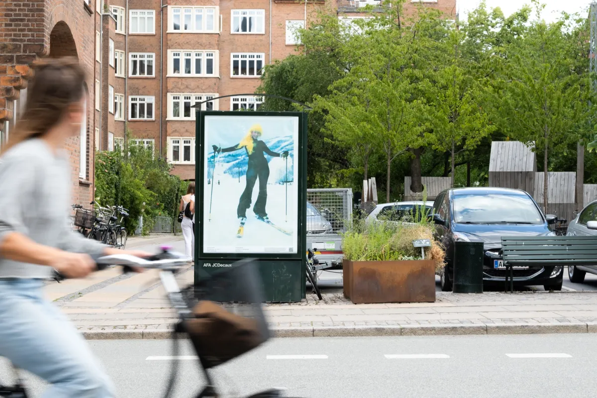 A small vertical billboard featuring an image of a person with yellow hair on skis.