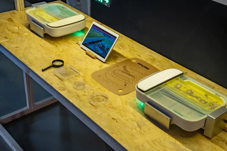 Close-up of a lab setup with magnifying glass, tablet, and experiment kit.