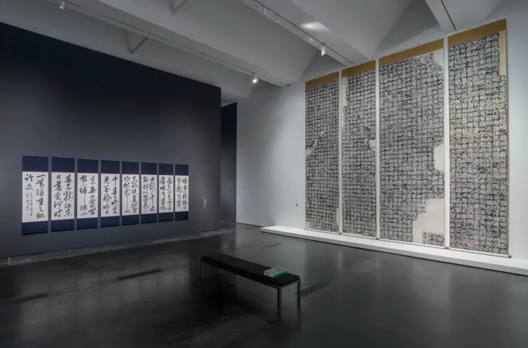 Exhibition gallery at Los Angeles County Museum of Art, featuring art pieces hung on walls, a dark flooring, and a central...