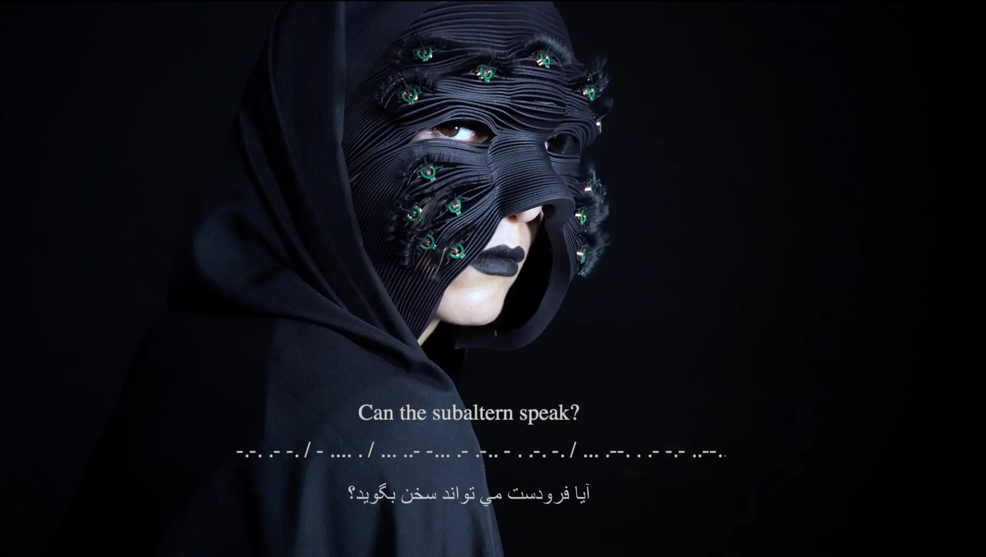 A person wearing a black mask with electronic elements and green lights, posing against a dark background with the question "Can the subaltern speak?" in English and Arabic.
