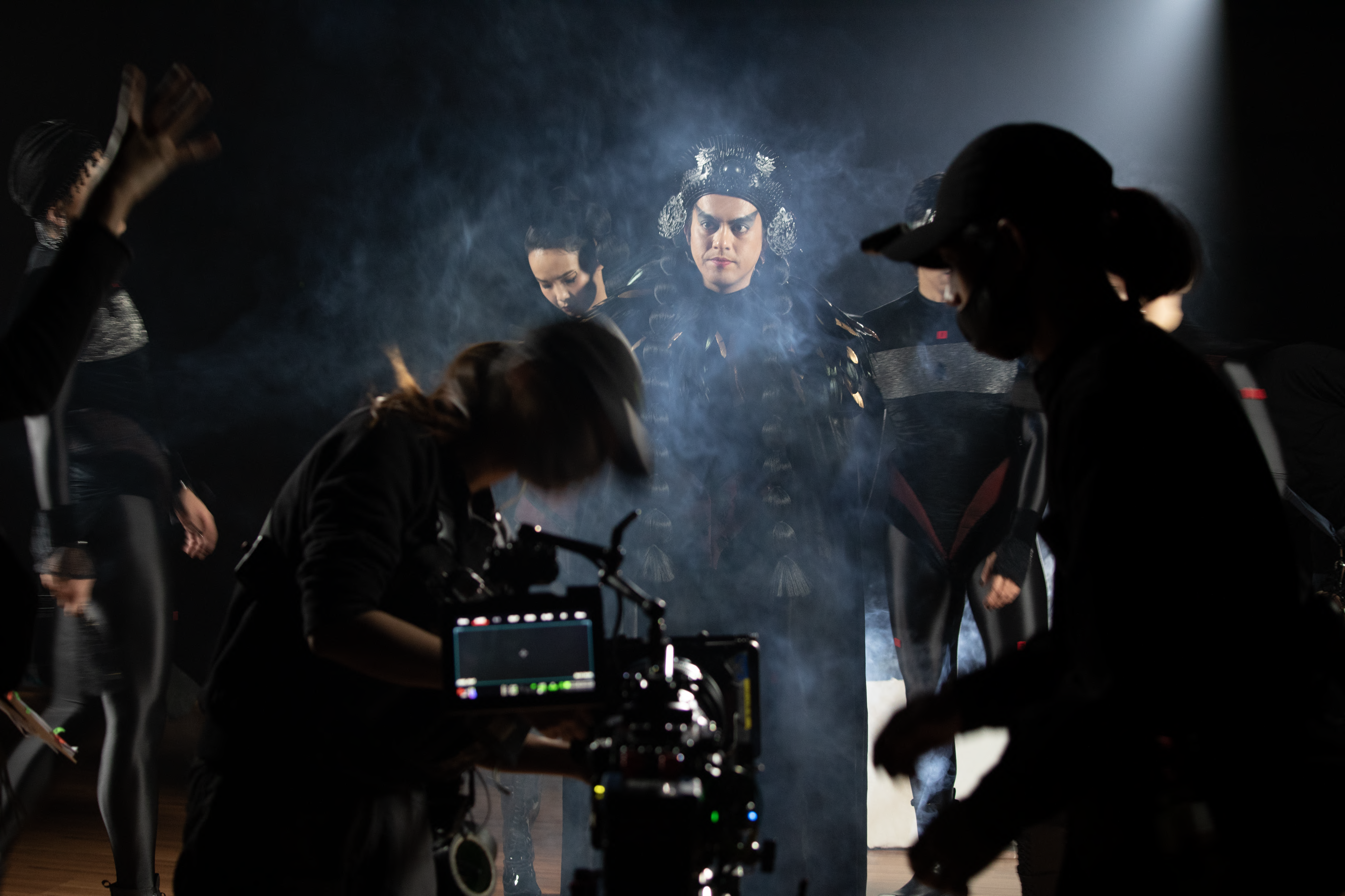 A performer stands center-stage during a recording session, surrounded by a myriad of individuals engaged in various tasks...