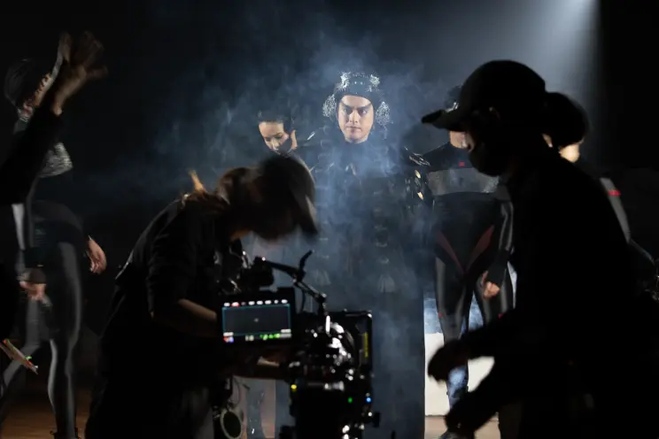 A performer stands center-stage during a recording session, surrounded by a myriad of individuals engaged in various tasks...