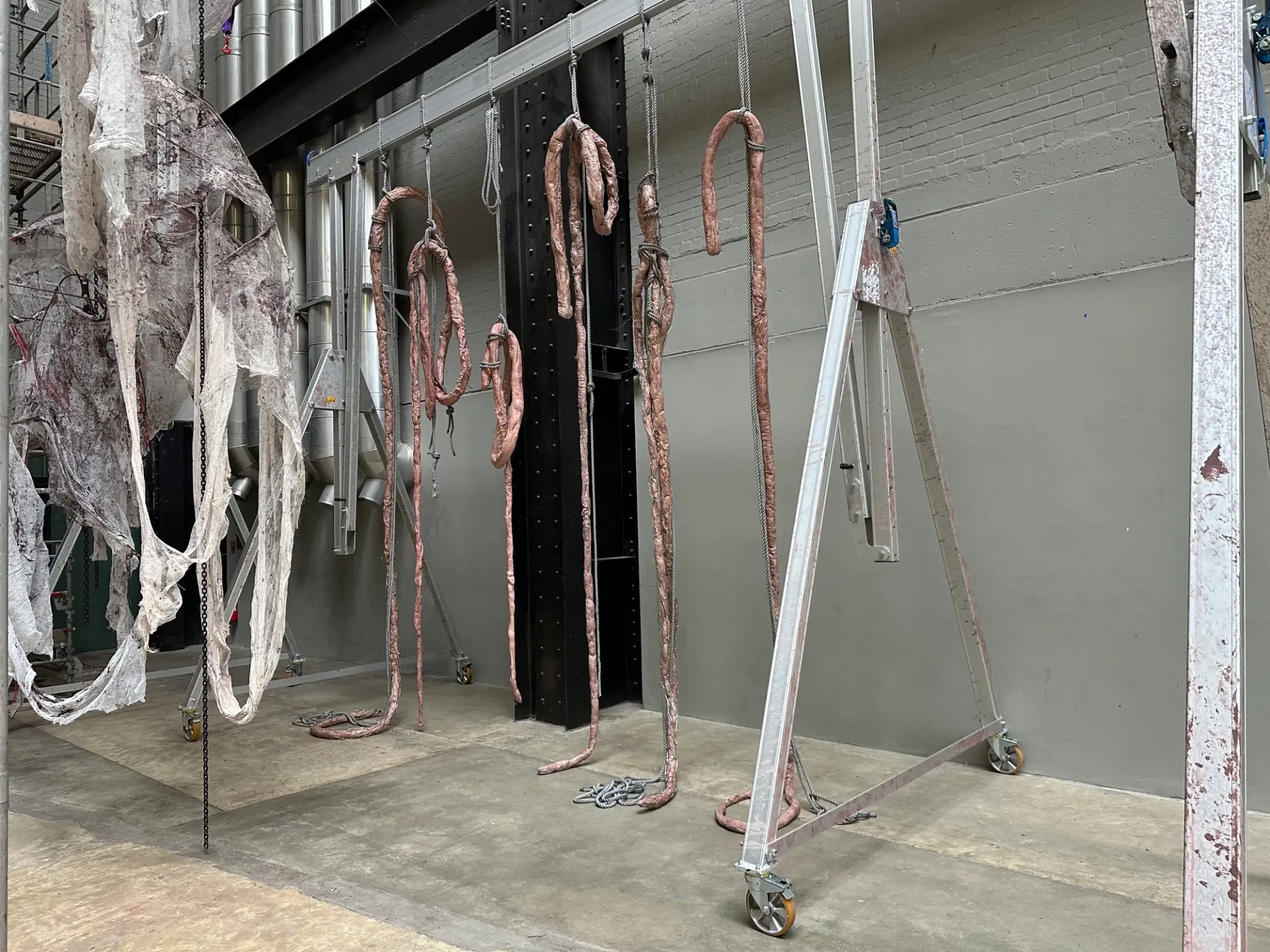Close-up of hanging fabric-like sculptures, with metallic hooks and ropes adding an industrial touch.
