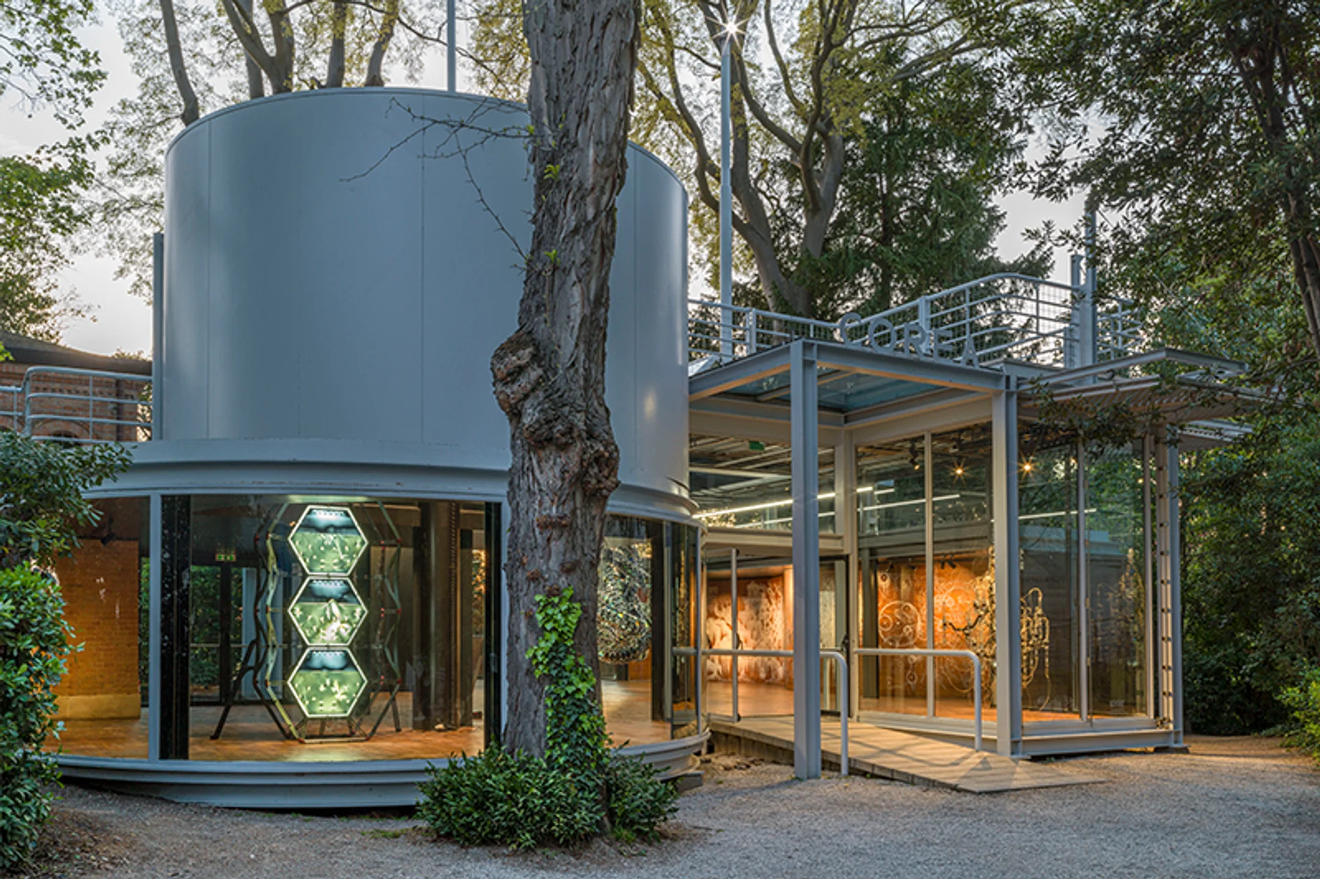 A cylindrical exhibition showroom stands outdoors, surrounded by other exhibition rooms nestled amid nature.