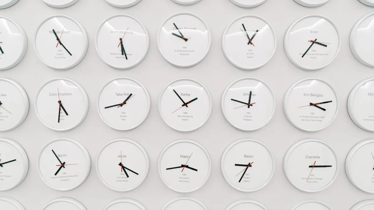 A white wall is densely populated with round clocks, each displaying a different time, indicative of various world time zones.