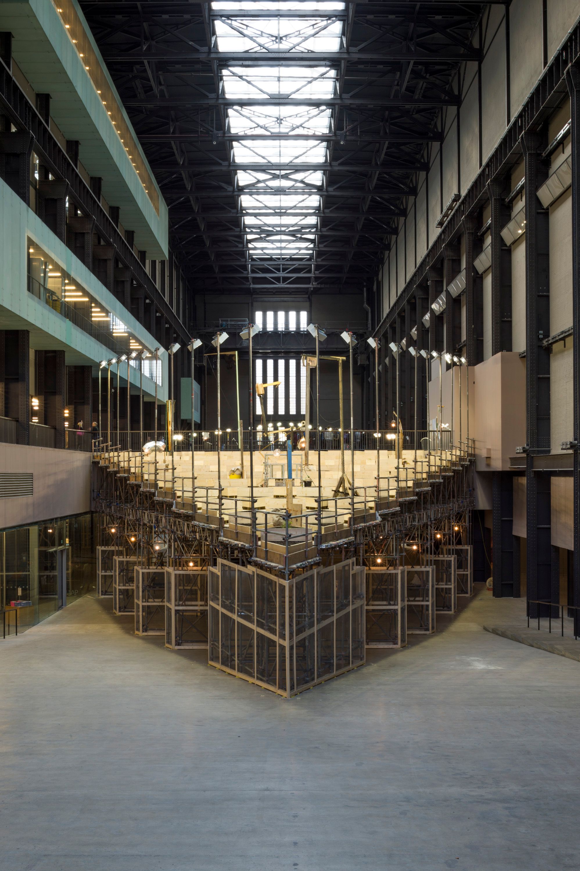 A vast art installation, of a garden fills a gallery space. The exhibit features an assortment of plants of varying sizes ...