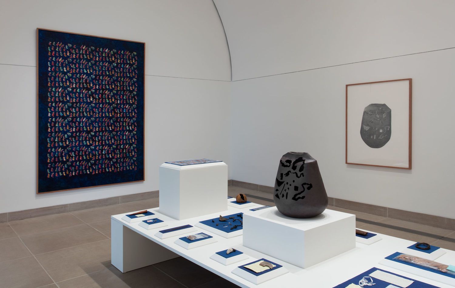 An art exhibition displaying a collection of rocks, a vessel/scultpure, and framed artworks on the wall.