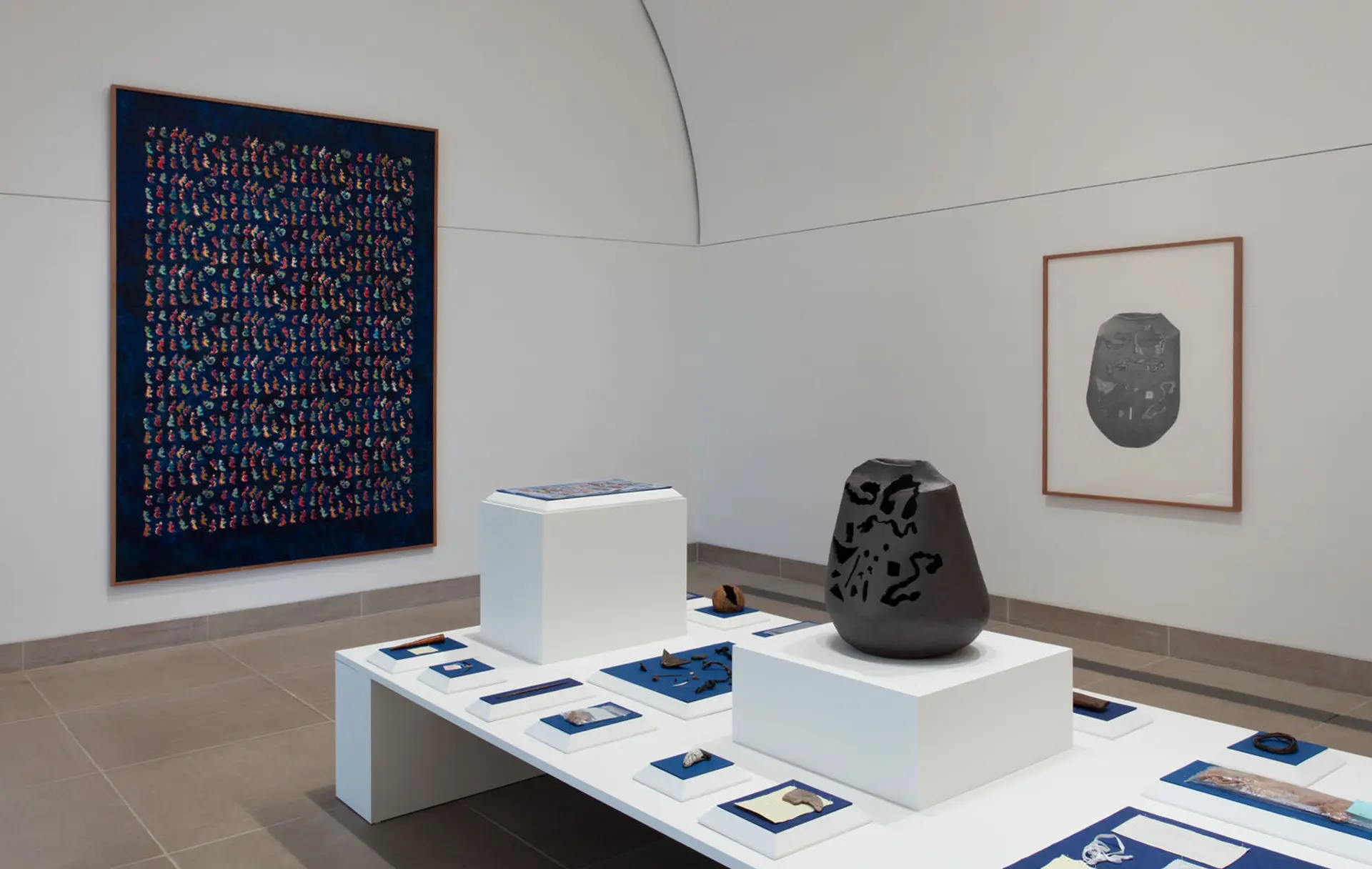 An art exhibition displaying a collection of rocks, a vessel/scultpure, and framed artworks on the wall.