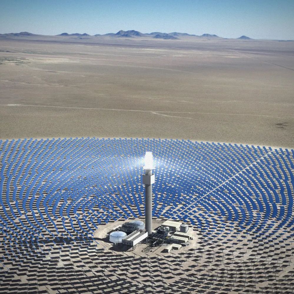 An aerial view of a large renewable energy installation, Solar Reserve, in Tonopah, Nevada. Thousands of photovoltaic panels are arranged in a circular pattern in a vast valley, reflecting bright sunlight.
