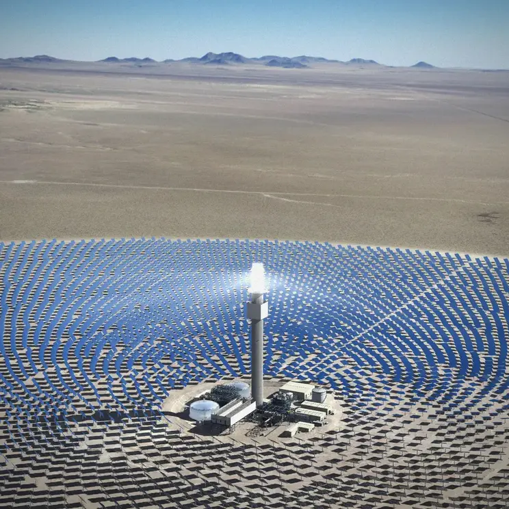 An aerial view of a large renewable energy installation, Solar Reserve, in Tonopah, Nevada. Thousands of photovoltaic panels are arranged in a circular pattern in a vast valley, reflecting bright sunlight.