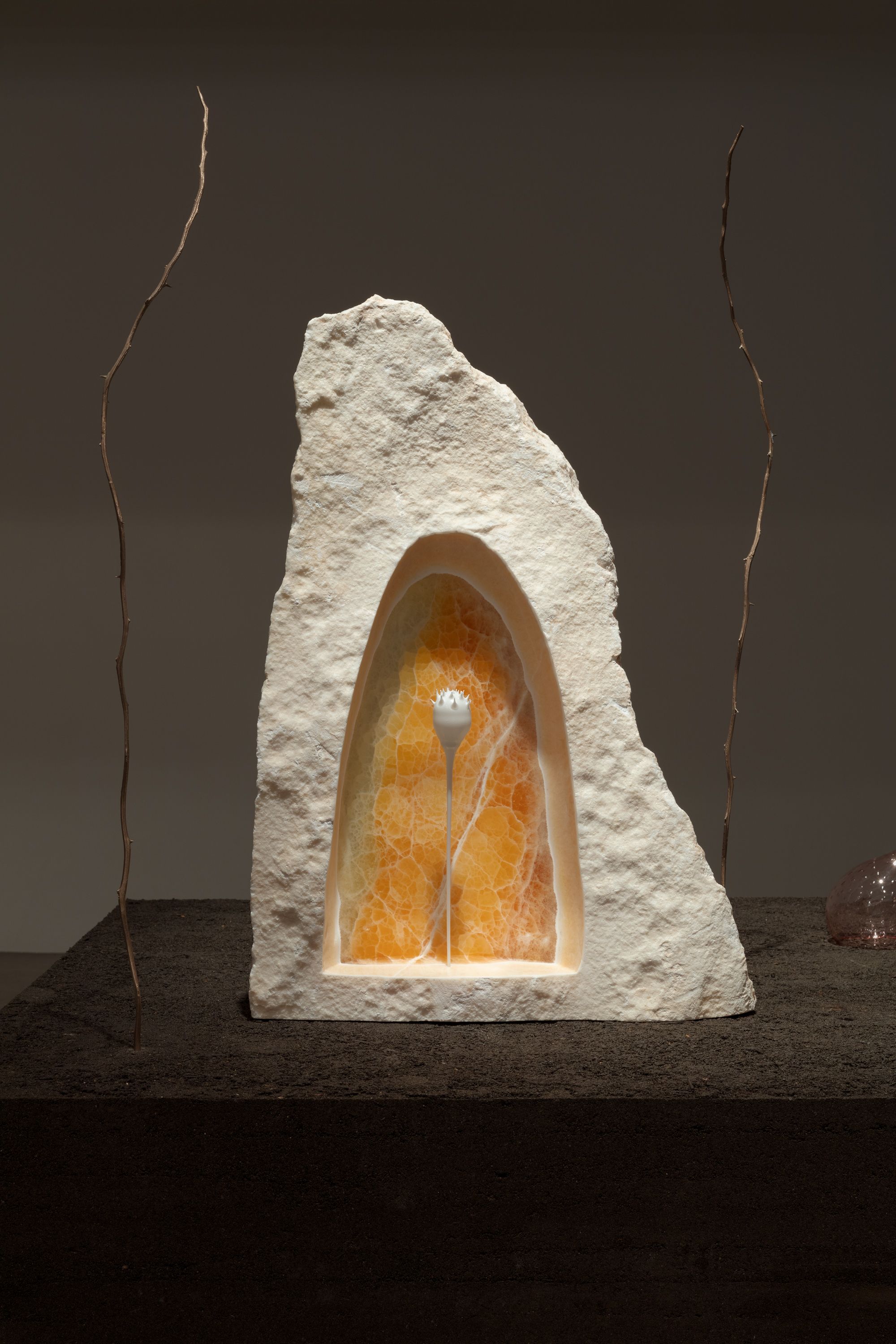 A cave-like white rock with amber interior. Twigs adorn the sides against a brown background.