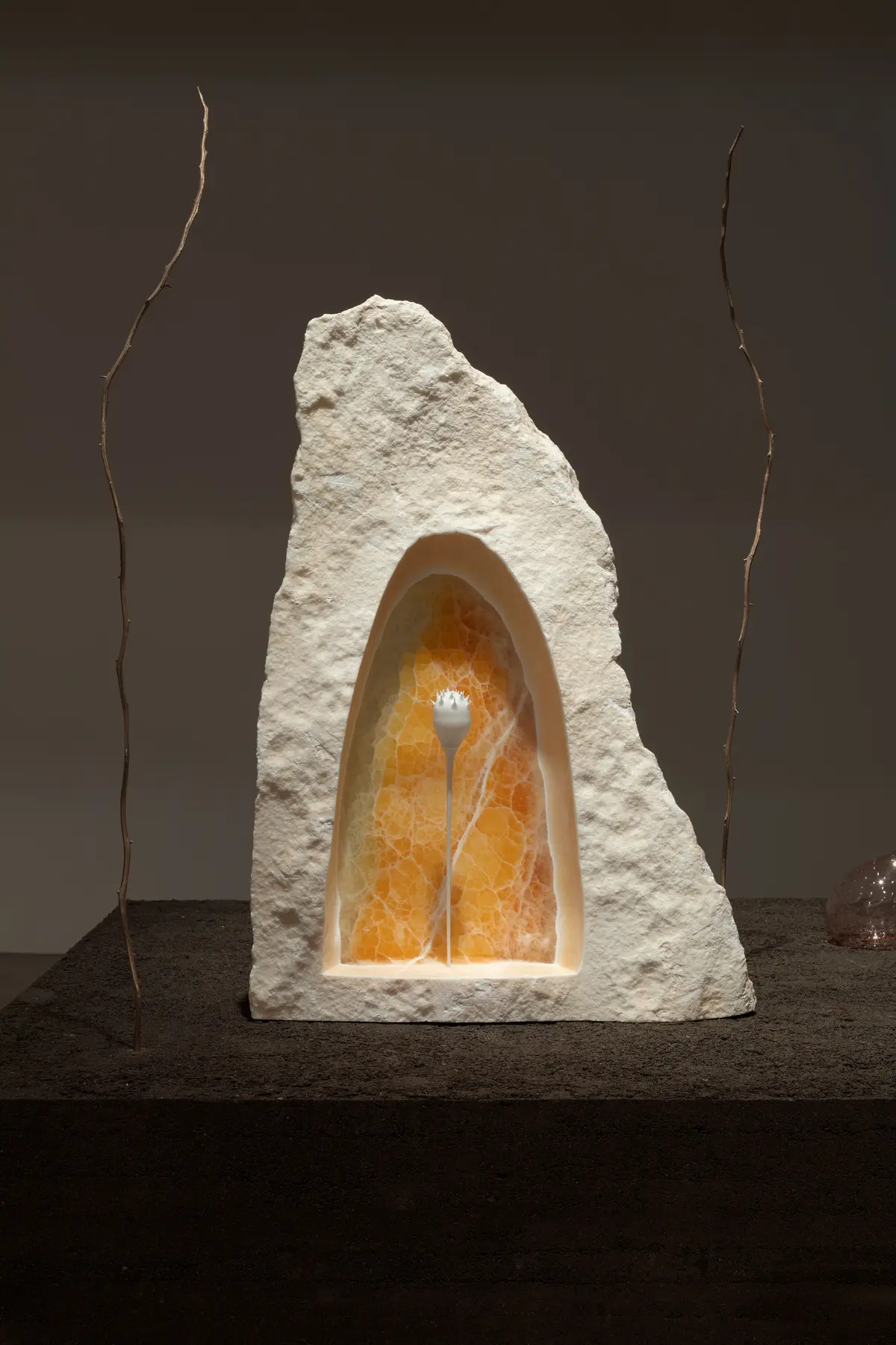 A cave-like white rock with amber interior. Twigs adorn the sides against a brown background.