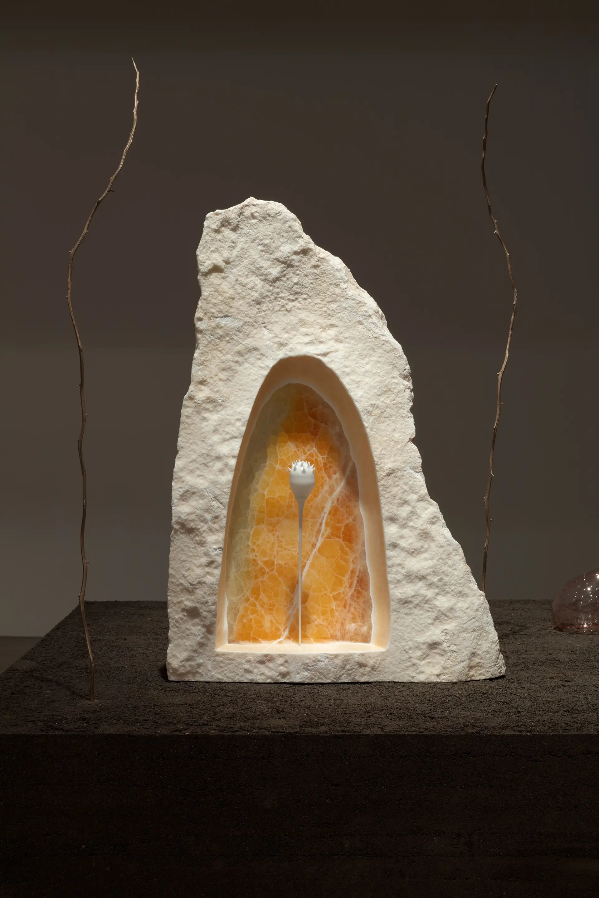 A cave-like white rock with amber interior. Twigs adorn the sides against a brown background.