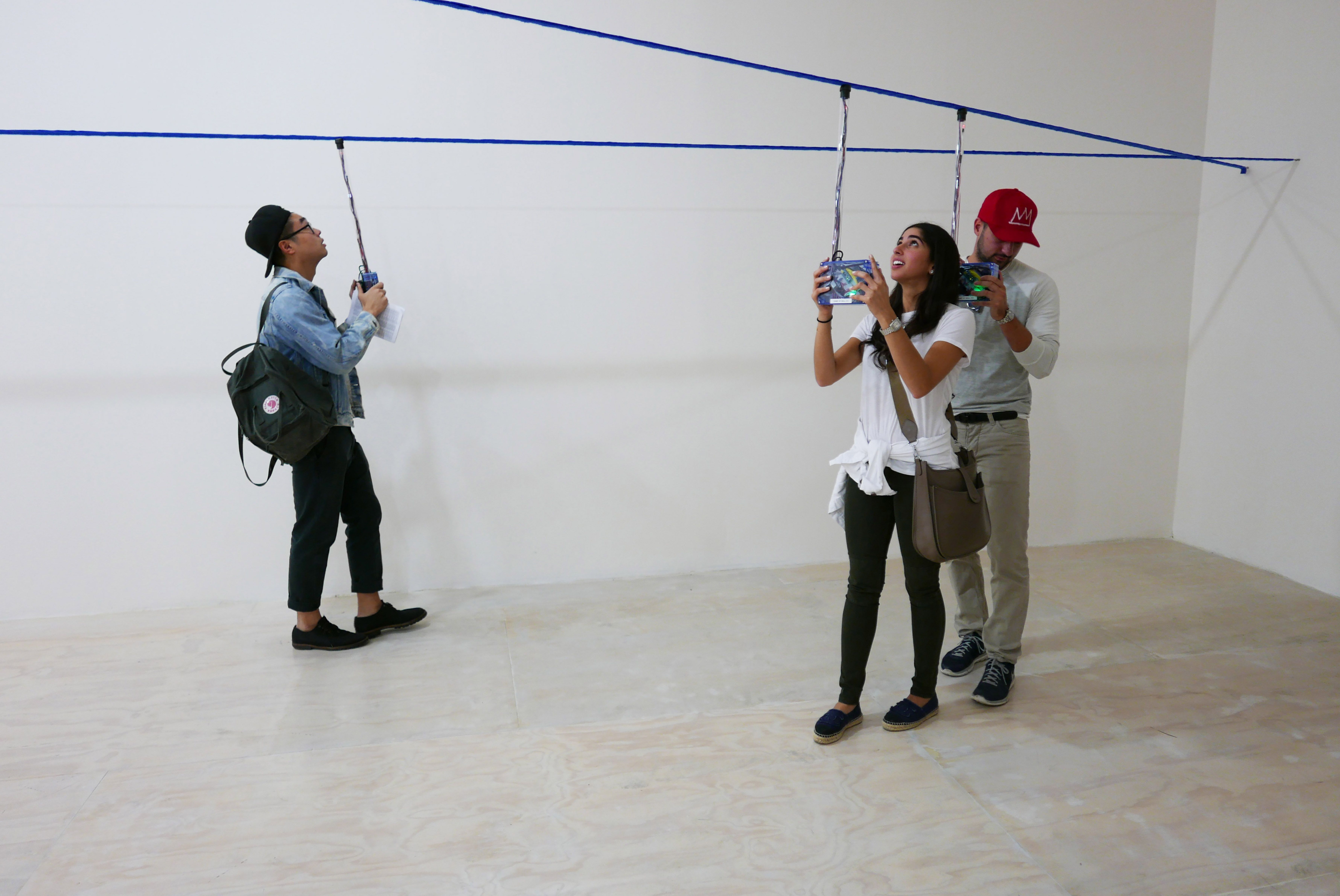 People interact with suspended blue electronic boxes in a gallery installation.