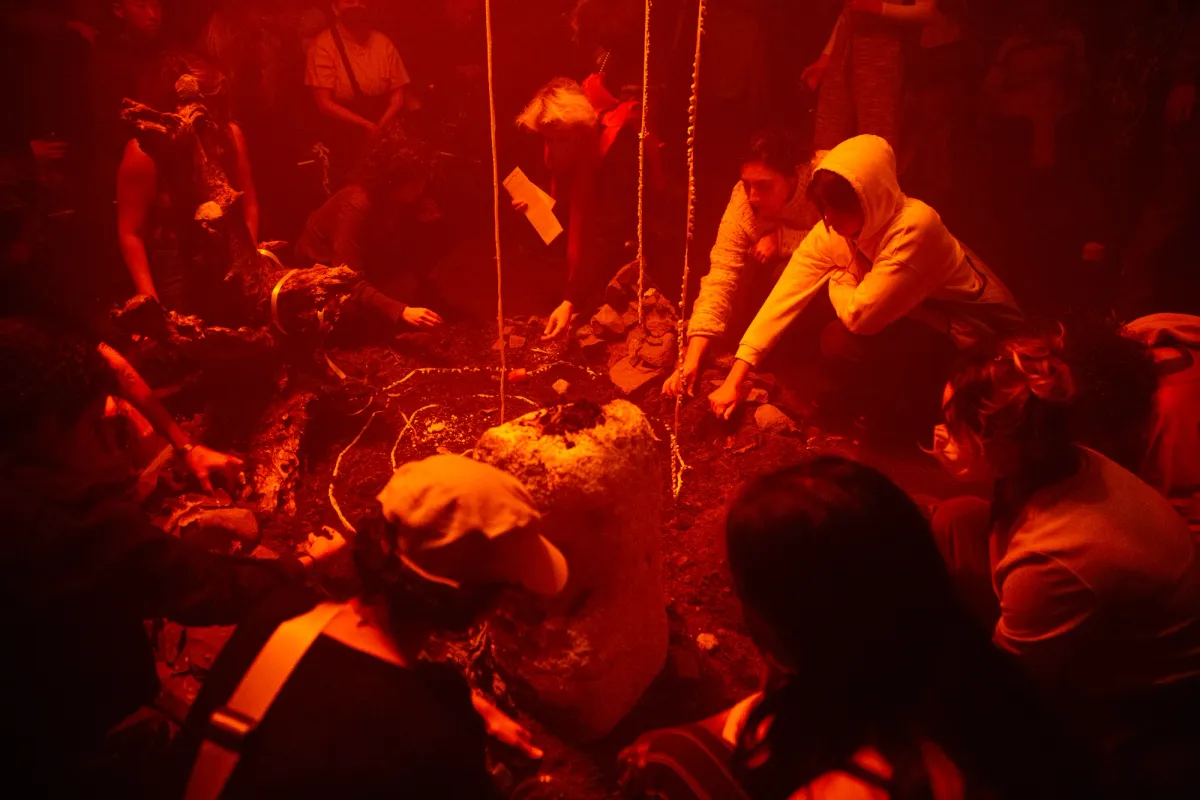 A group of people standing and crouching around a pile of soil under red lights.