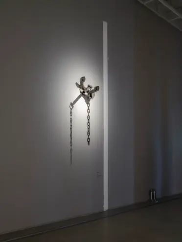 An anchored wall under a spotlight, with a broken chain hanging from the anchor, viewed in a dimmed environment.