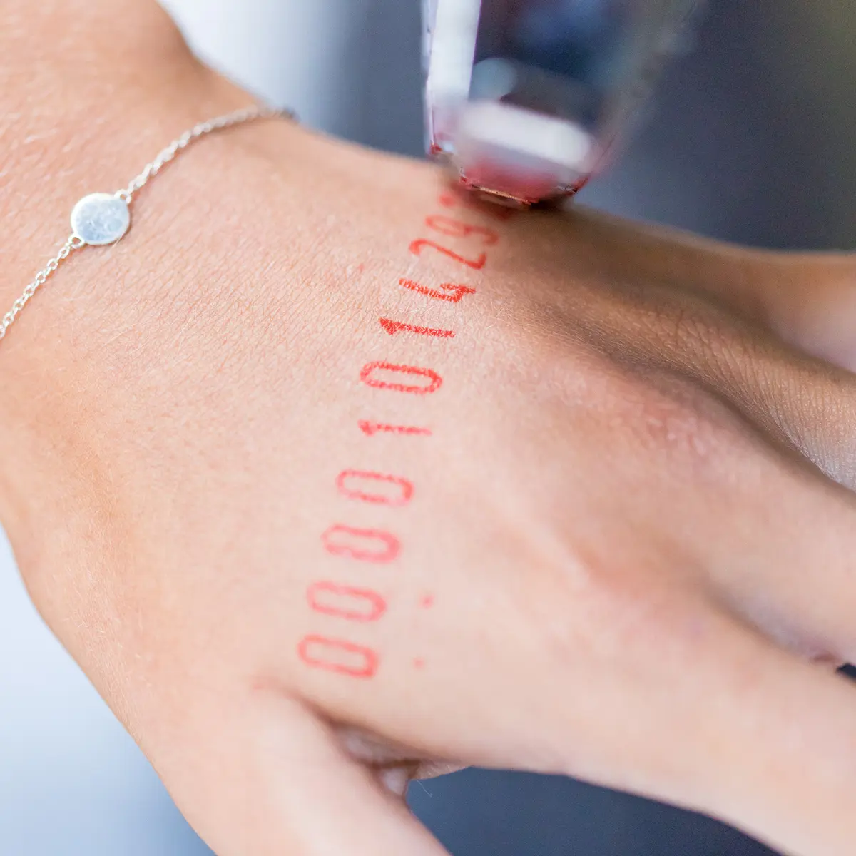 A hand is being stamped with red ink, imprinting a series of numbers onto the skin.