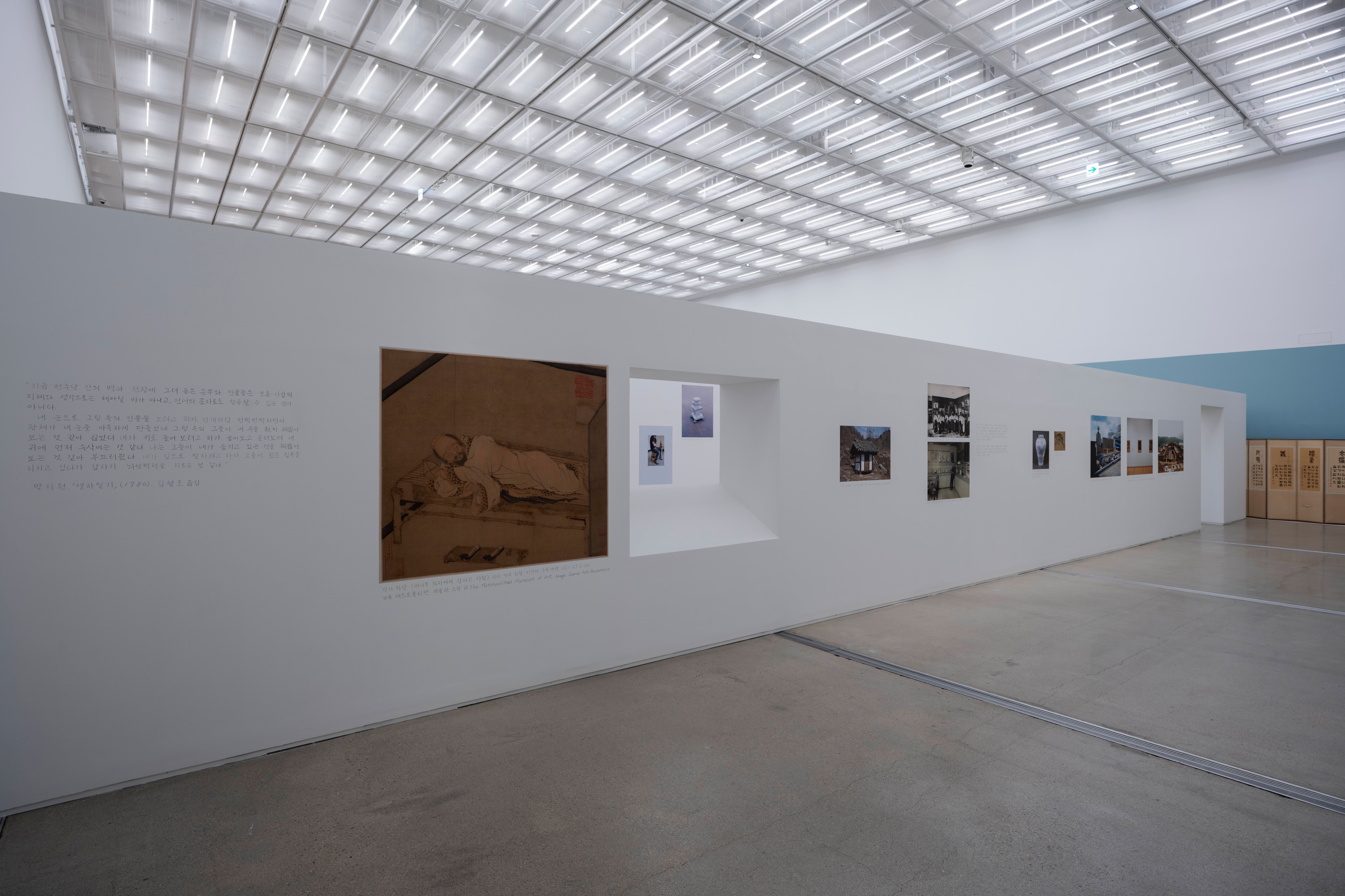Artwork is displayed in a well-lit gallery with a large, white wall.
