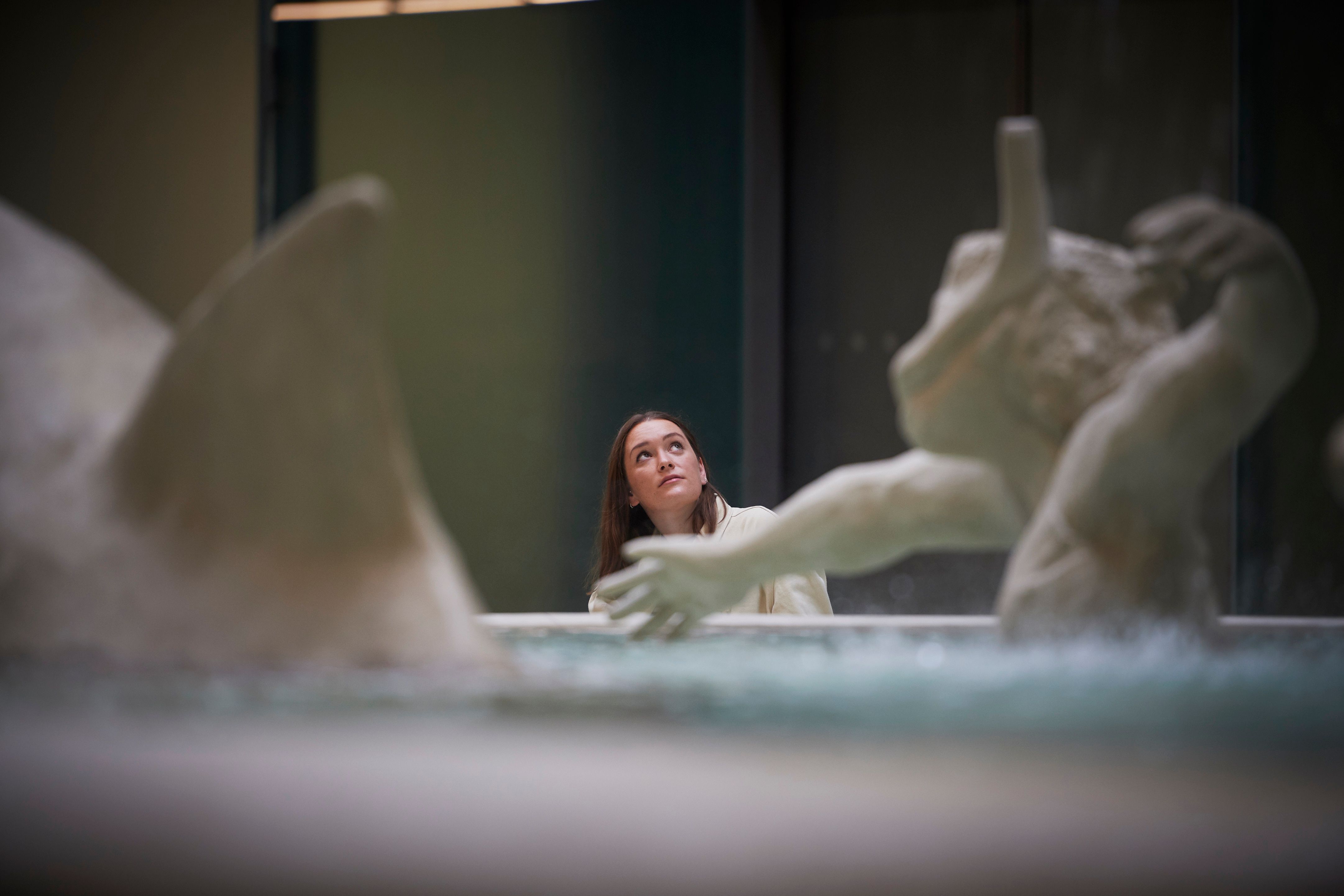 A person stands near the base of the monumental Fons Americanus fountain inside the Tate Modern, looking up towards the to...