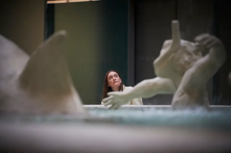 A person stands near the base of the monumental Fons Americanus fountain inside the Tate Modern, looking up towards the to...