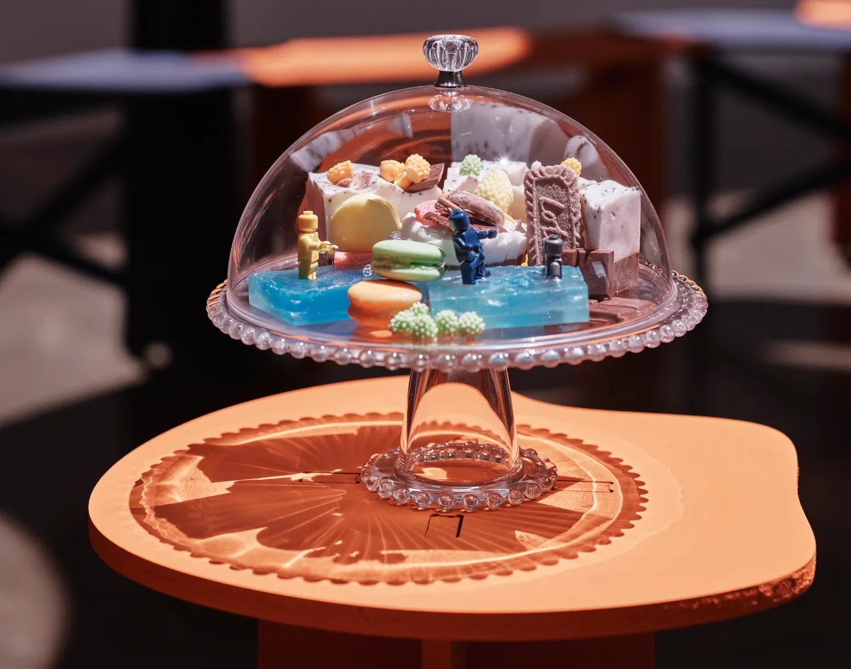 Assorted sweets showcased on a glass stand with cover, situated on an wood coffee table.