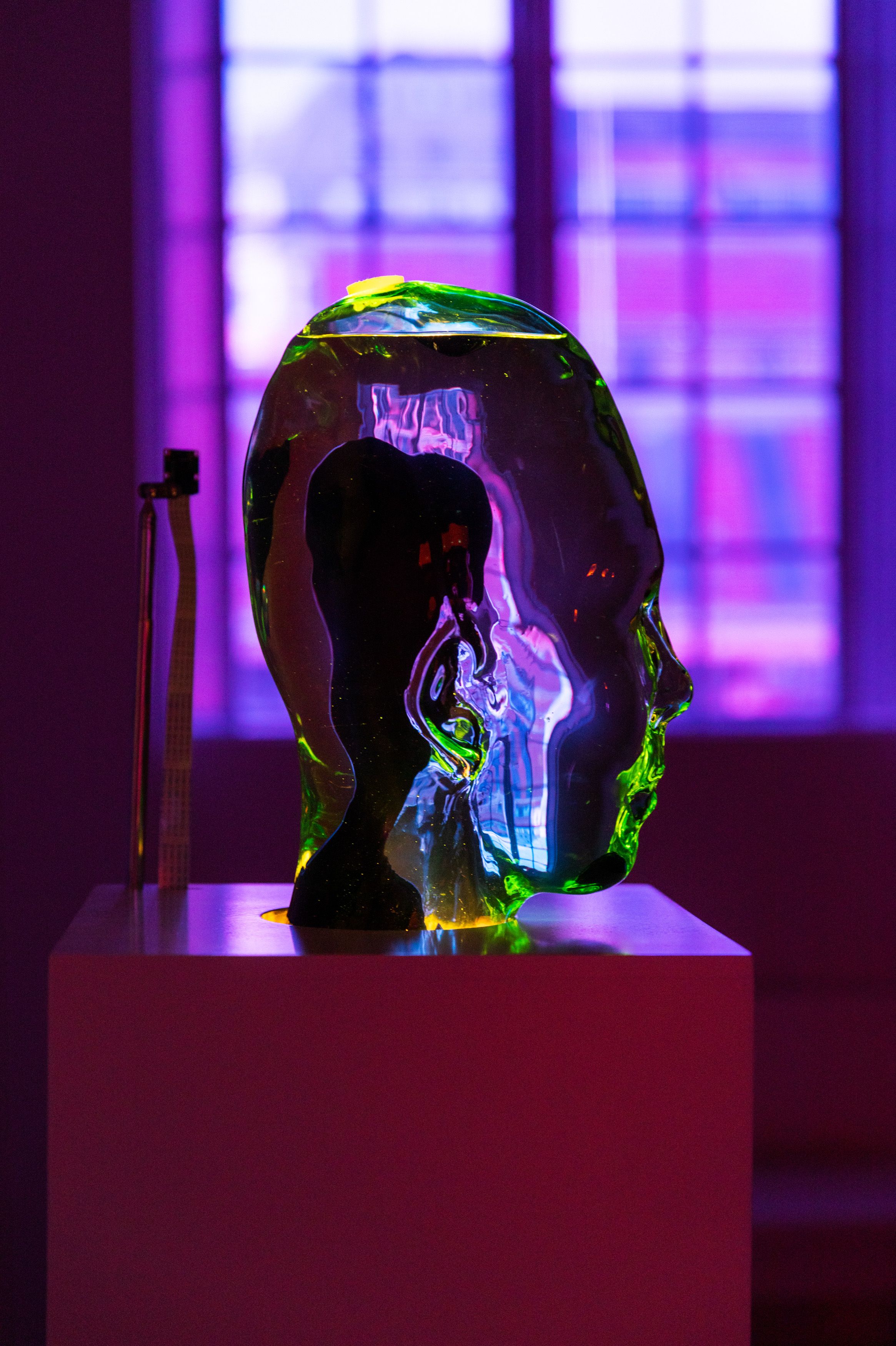A glowing translucent head-shaped sculpture in green and yellow hues illuminated against purple window light.