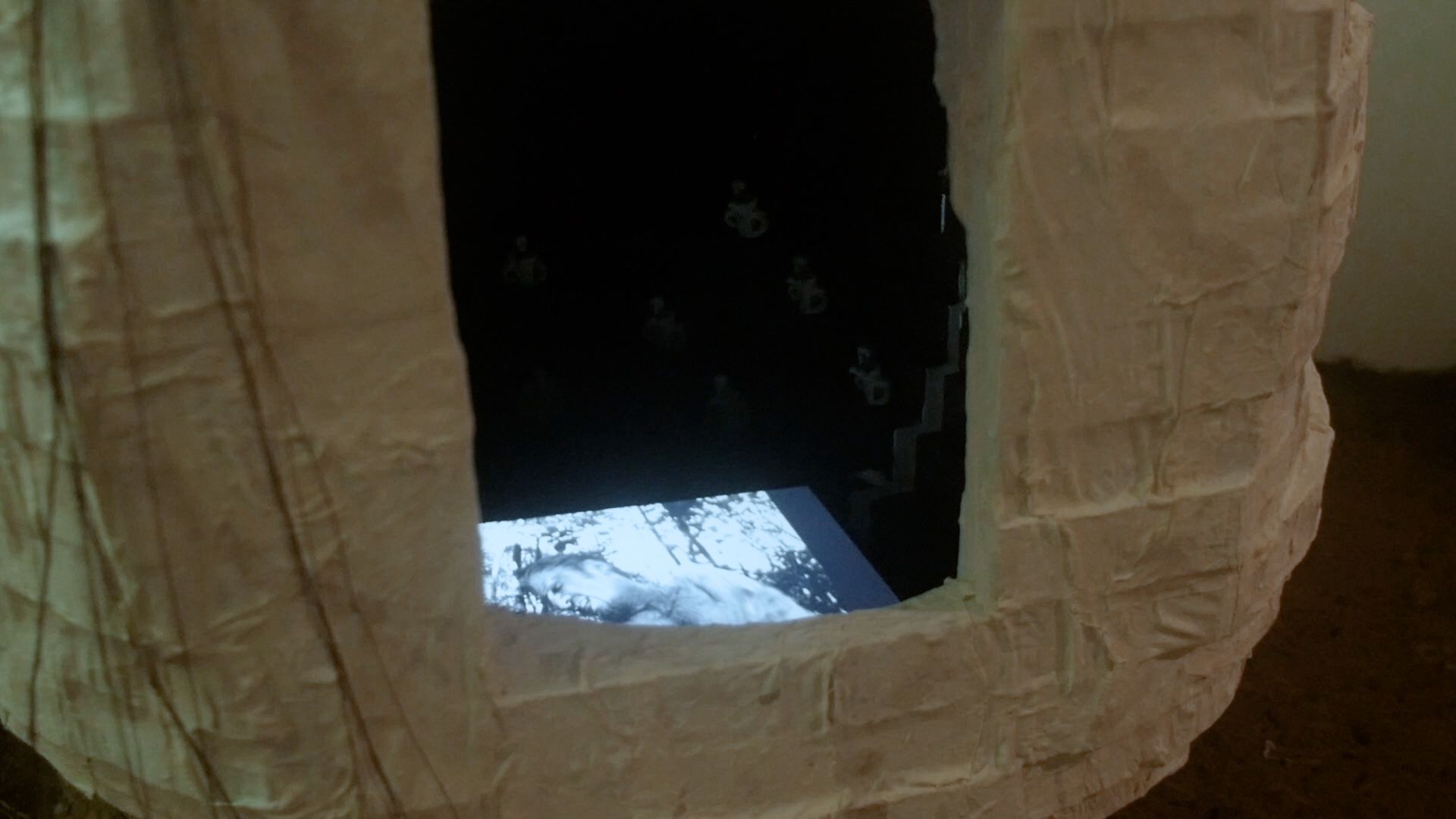 A white, dome-shaped structure with a square opening reveals a black-and-white video inside.