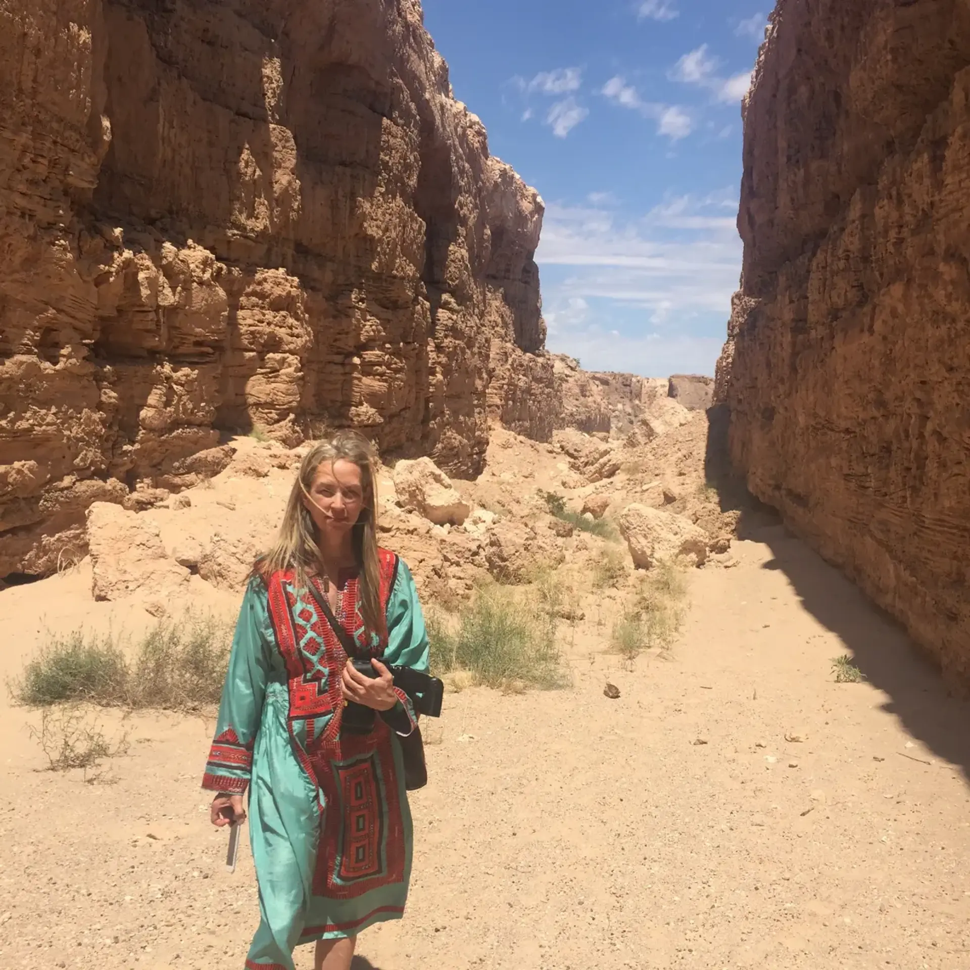 A person stands in a mountainous landscape under a cloud-filled sky, looking directly at the camera.