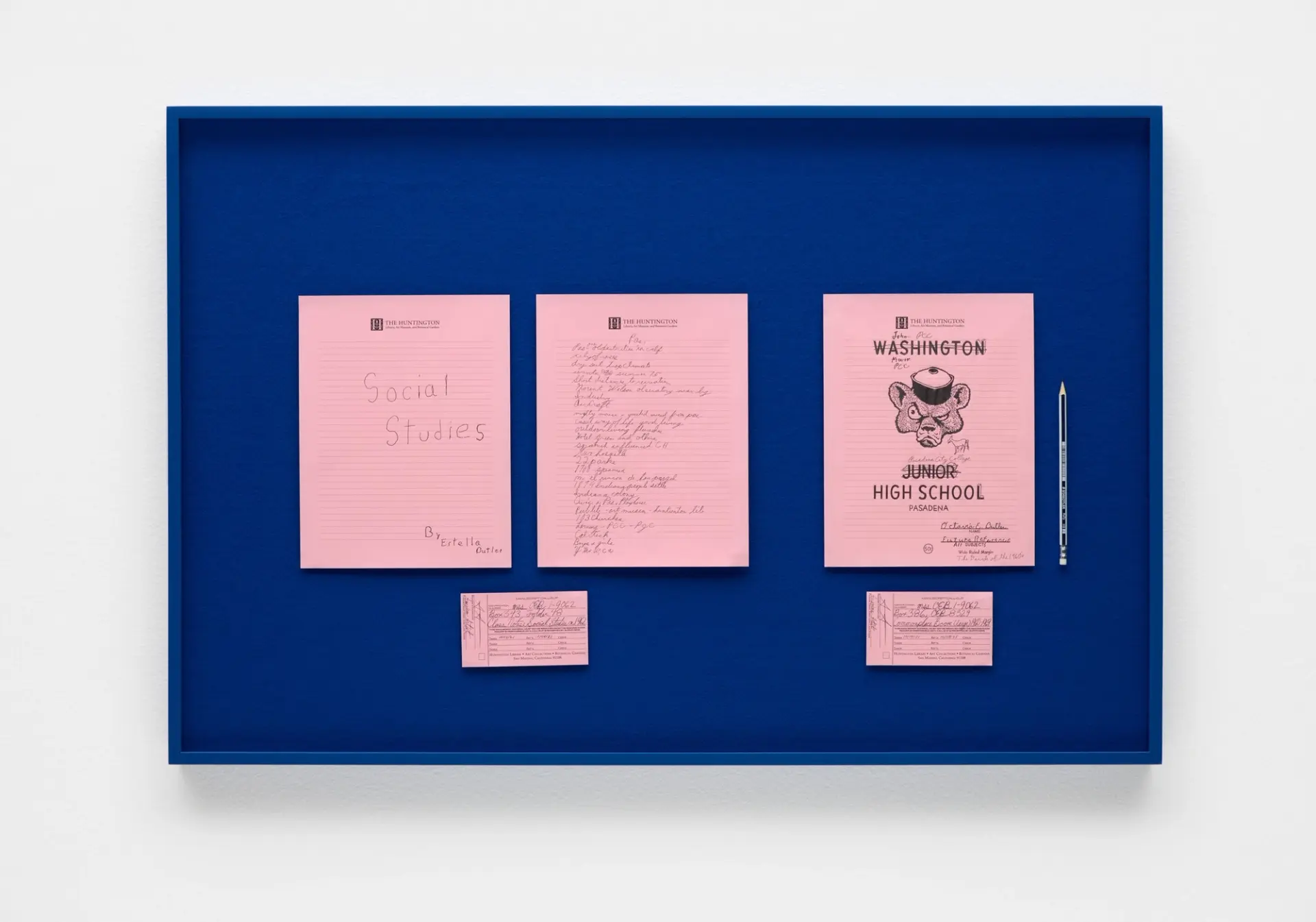 A blue display case holds three pink paper booklets labeled "Social Studies" and "Washington Junior High School," along with smaller pink paper slips and a pencil.