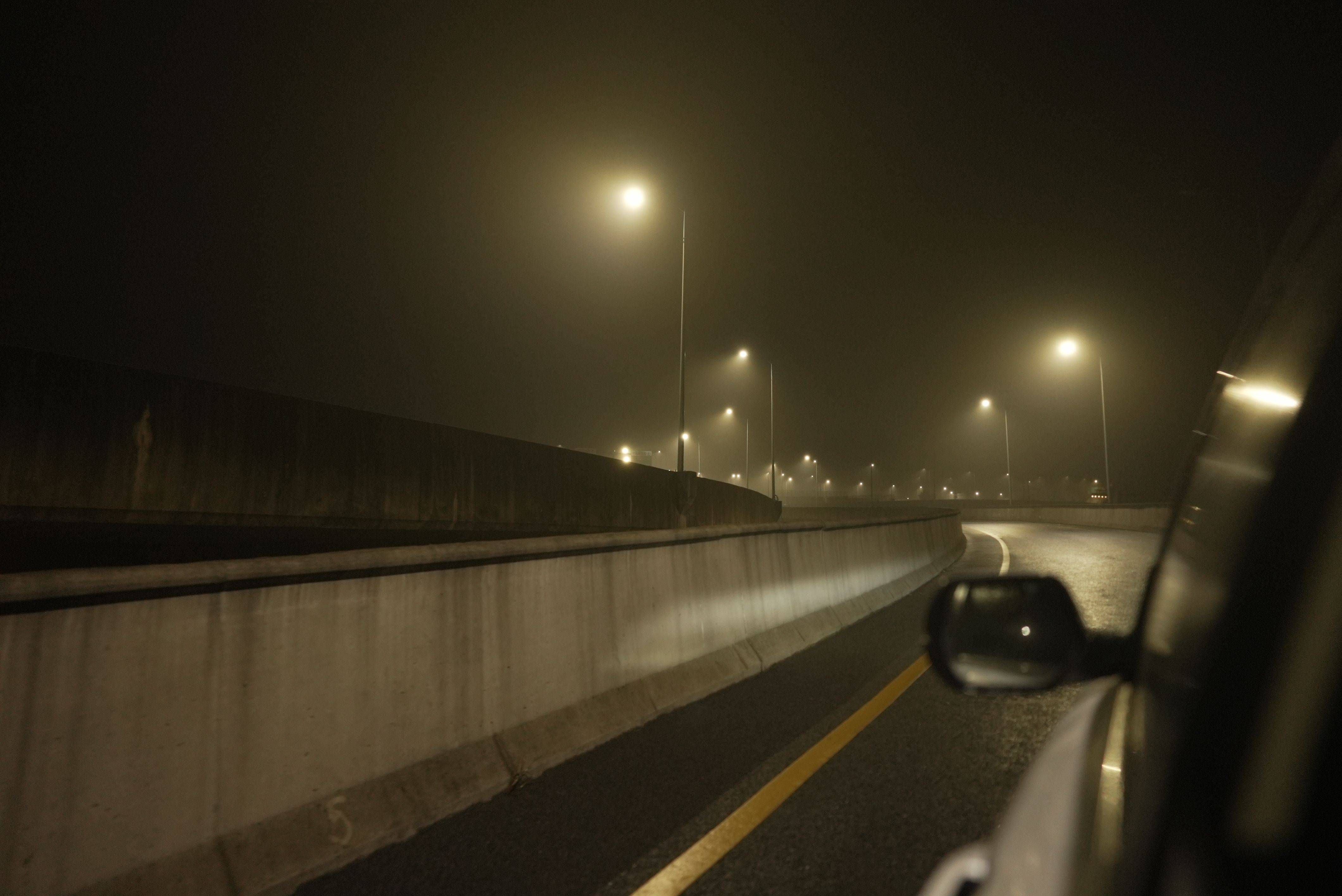A nighttime view from the backseat of a car, showcasing an illuminated road stretching into darkness.