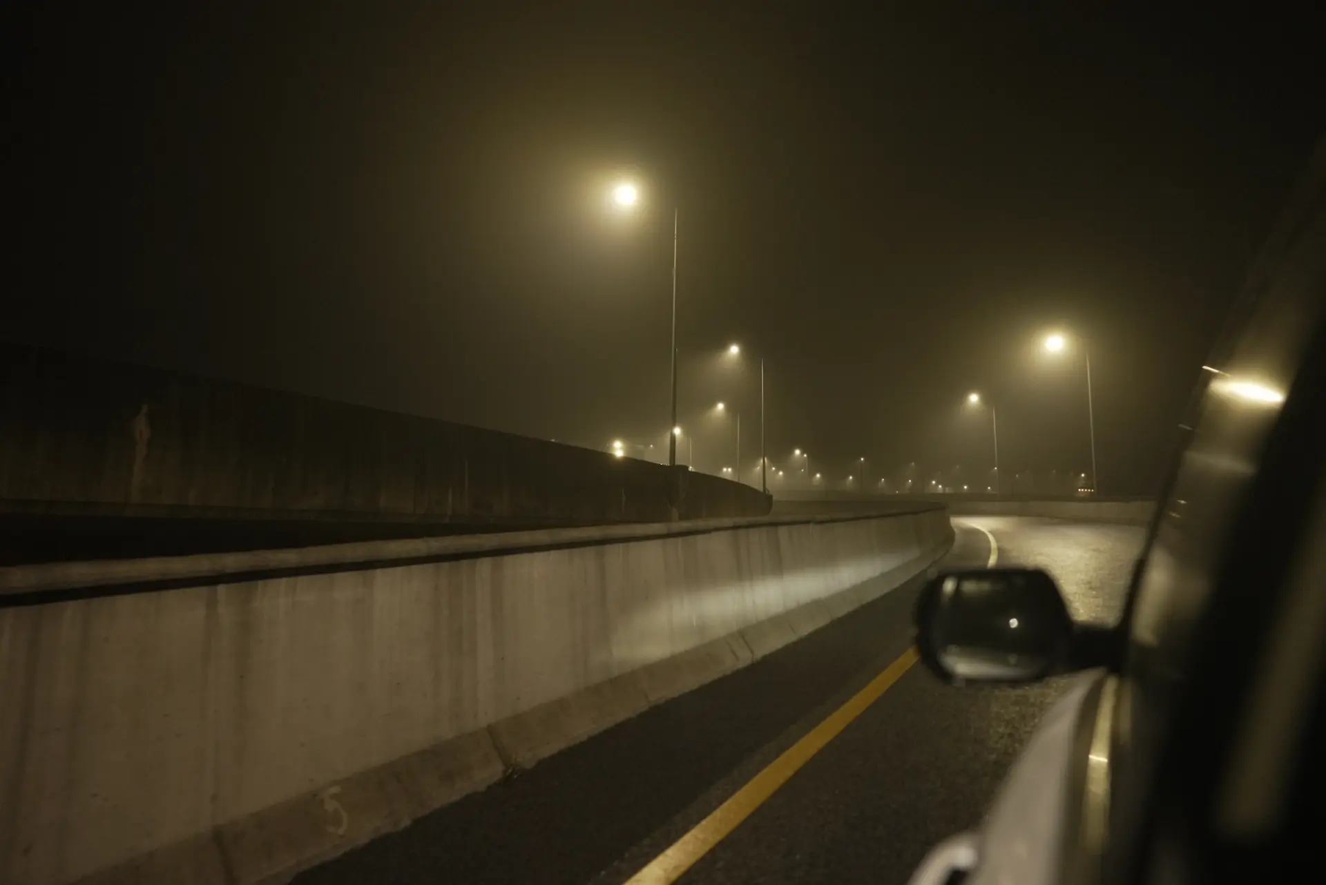 A nighttime view from the backseat of a car, showcasing an illuminated road stretching into darkness.