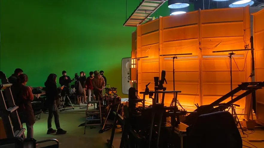 A dimly lit studio stage where professionals are working amongst a variety of equipment. An ambient, soft orange light ill...