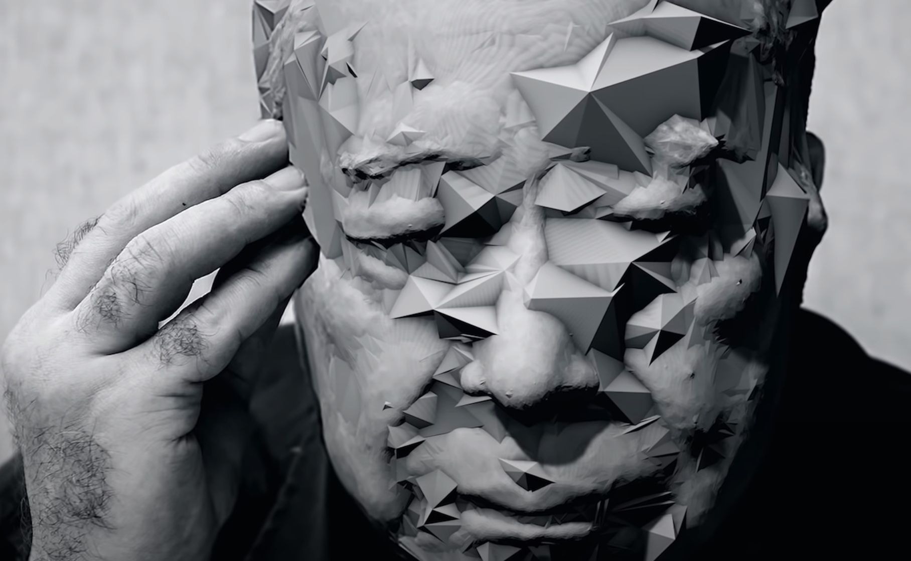 A black and white headshot of a person in deep thought, their face artistically overlaid with an abundance of 3D pyramids.