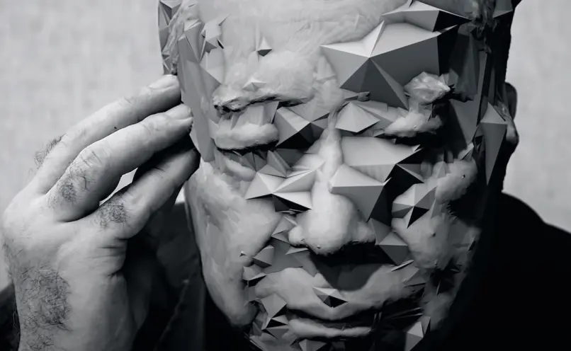 A black and white headshot of a person in deep thought, their face artistically overlaid with an abundance of 3D pyramids.
