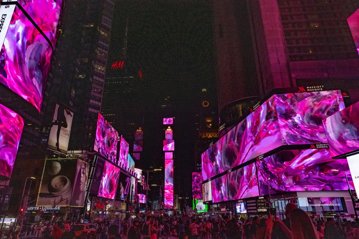 Times Square surrounded by buildings, with large advertisement screens displaying abstract pink art forms.