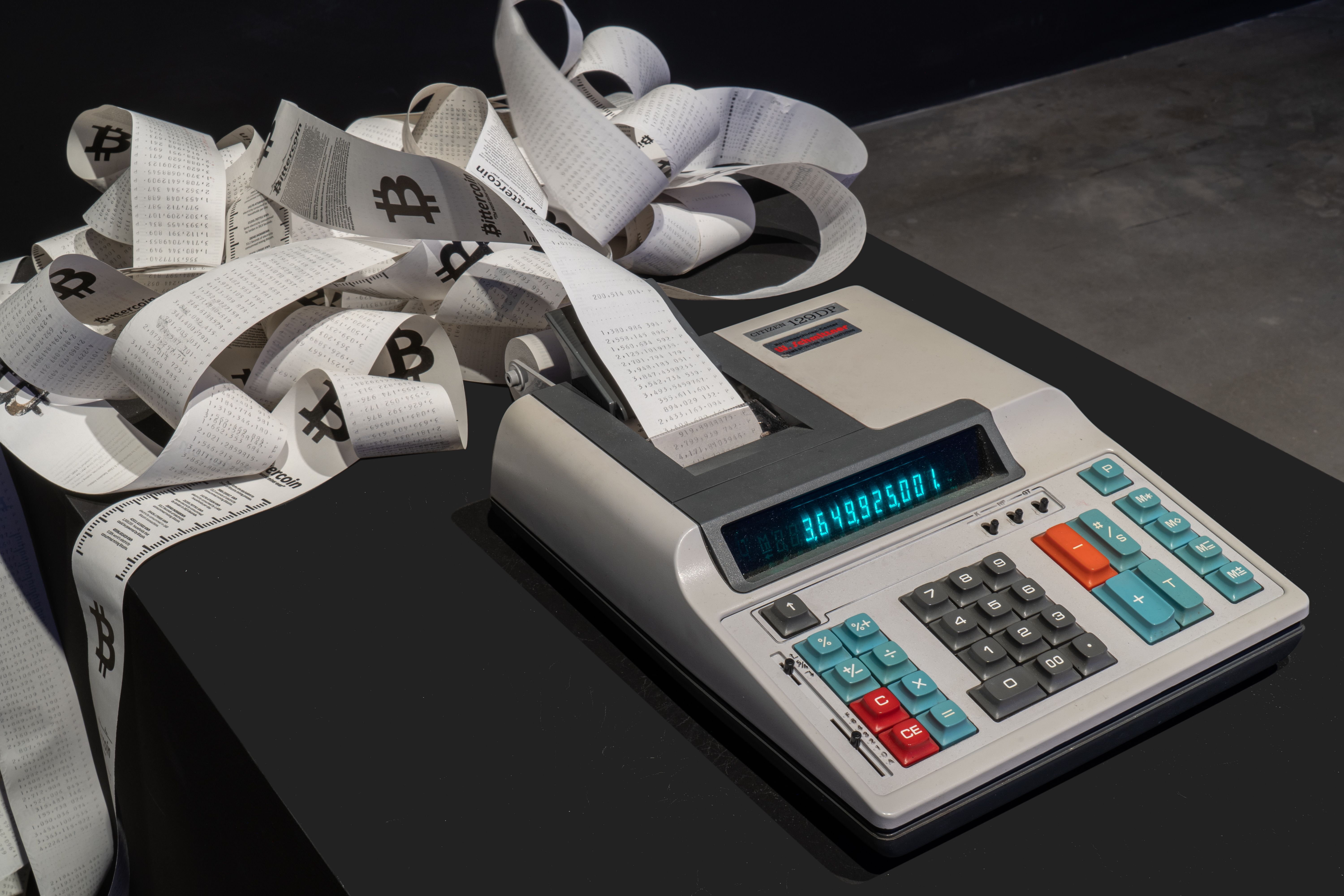 Artistic display of a calculator and paper rolls with cryptocurrency symbols.