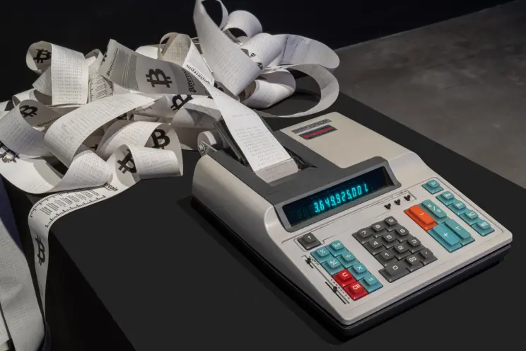Artistic display of a calculator and paper rolls with cryptocurrency symbols.