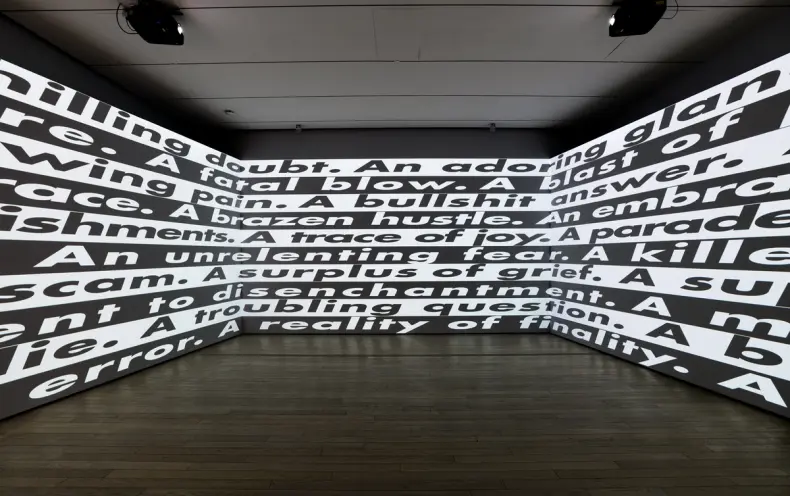 A large gallery space adorned with black and white text, presented in a reversed pattern across three extensive walls.