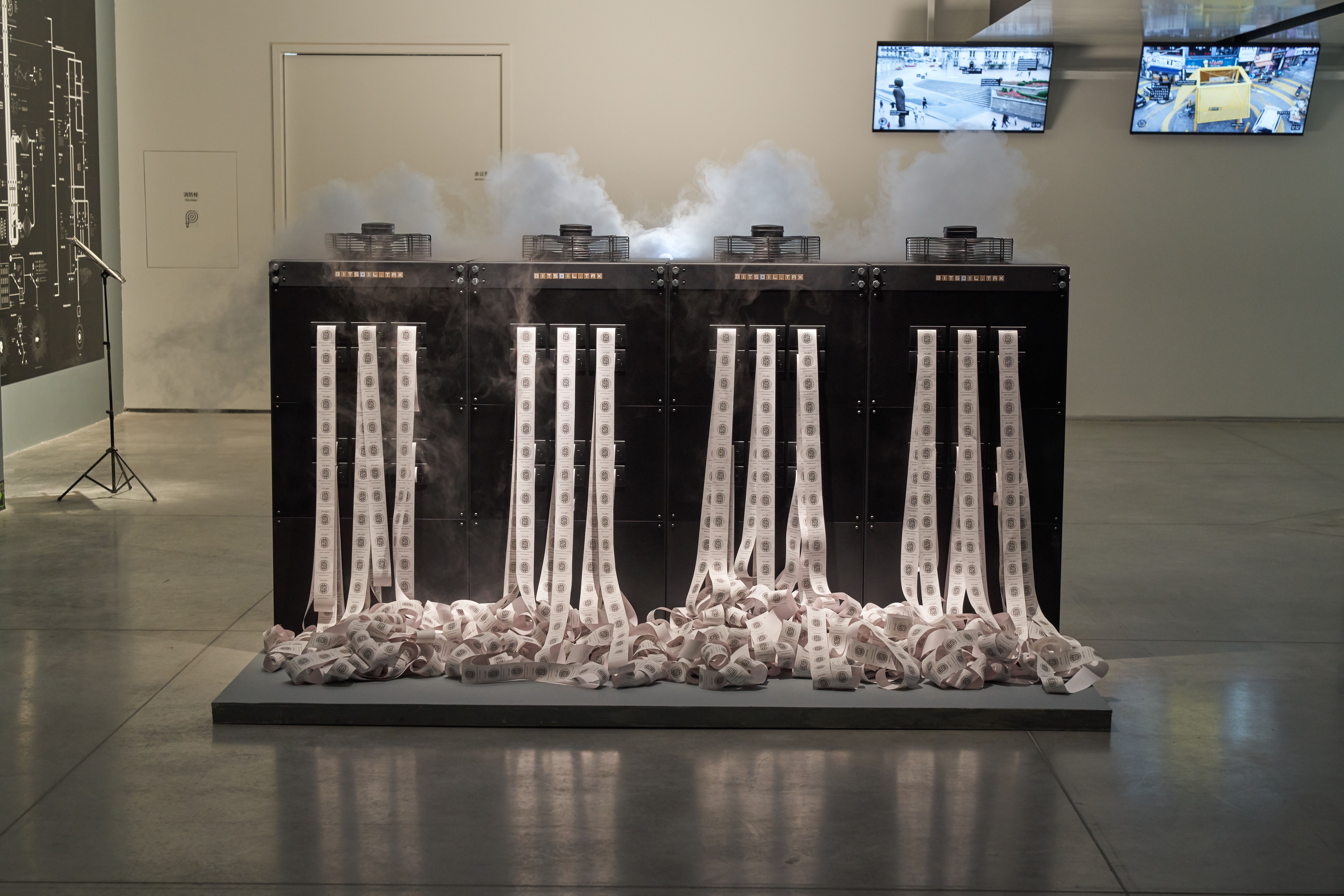 Printers emitting paper and smoke with screens in art exhibit.