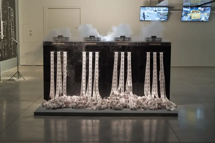 Printers emitting paper and smoke with screens in art exhibit.