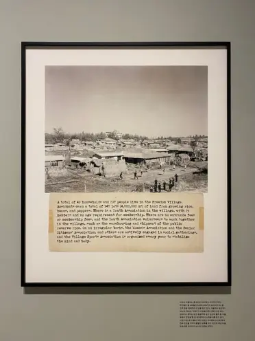 A vintage photograph of a town, depicted in black-and-white tones, mounted in a frame on the wall of an art gallery. The p...