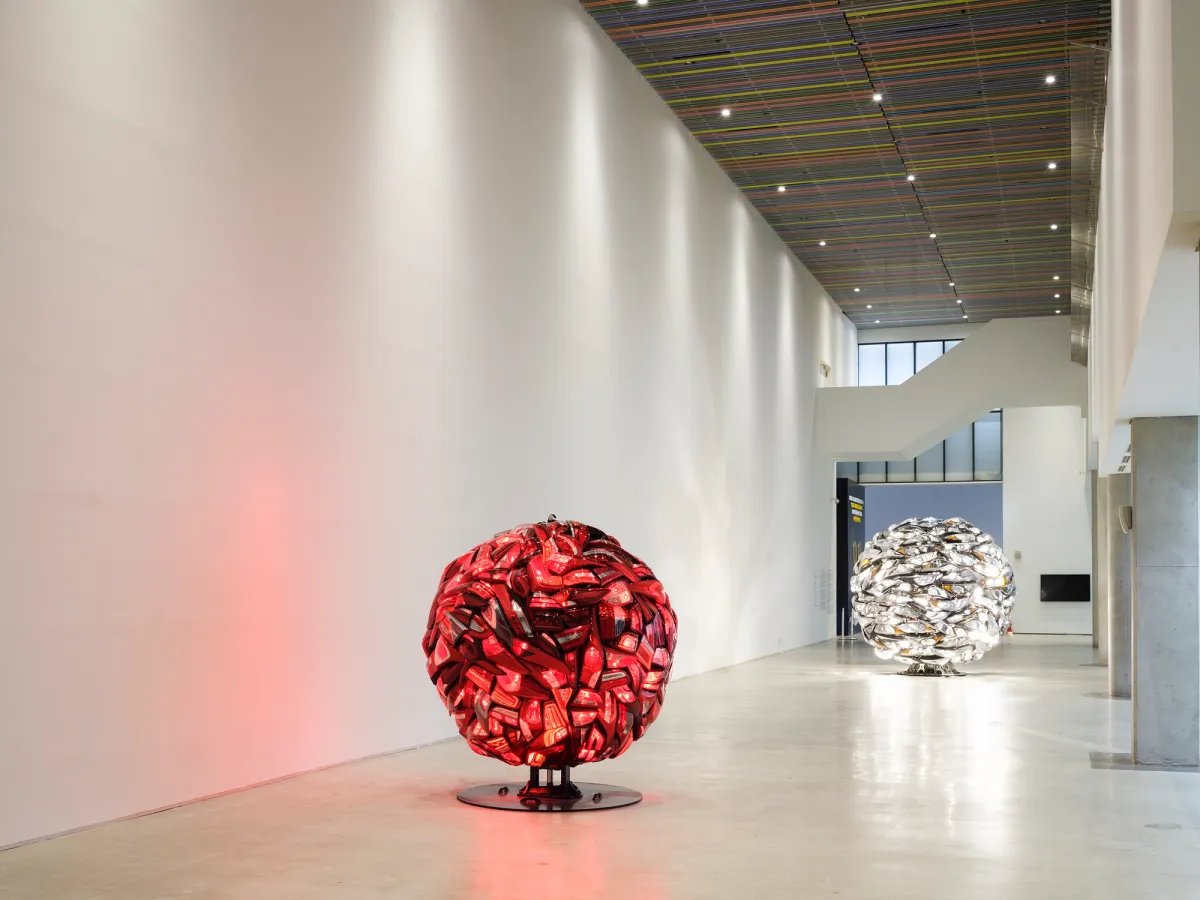 Two large, spherical sculptures, one in vibrant red and the other in pristine white, occupy a spacious area. Each sculpture is composed of Hyundai Motors headlights and taillights.