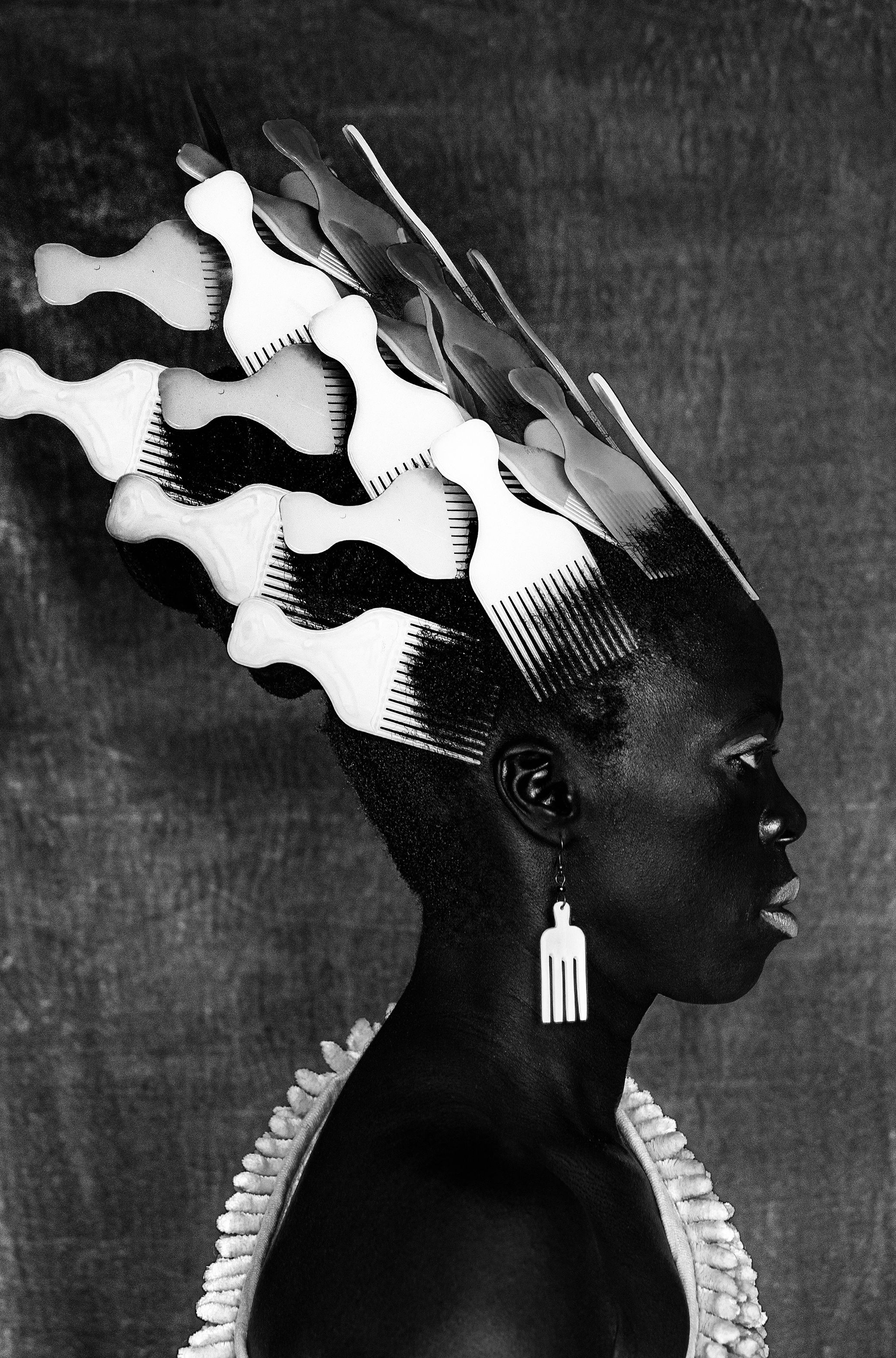 Black and white profile portrait of a person with numerous white combs inserted into their hair.