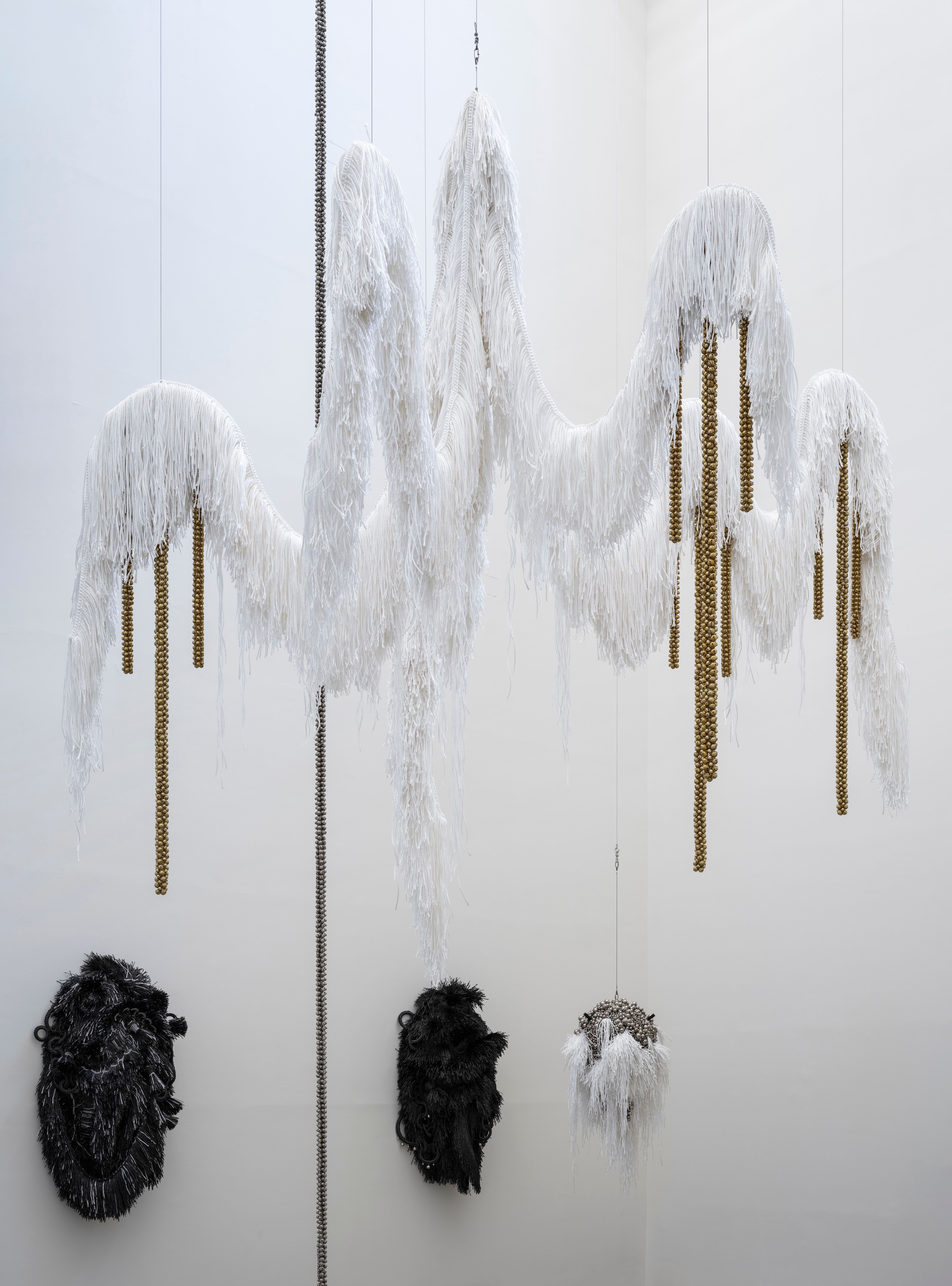 An art installation featuring a large, white, furry chandelier-like structure suspended from the ceiling. Adorning the wal...