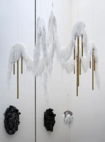 An art installation featuring a large, white, furry chandelier-like structure suspended from the ceiling. Adorning the wal...