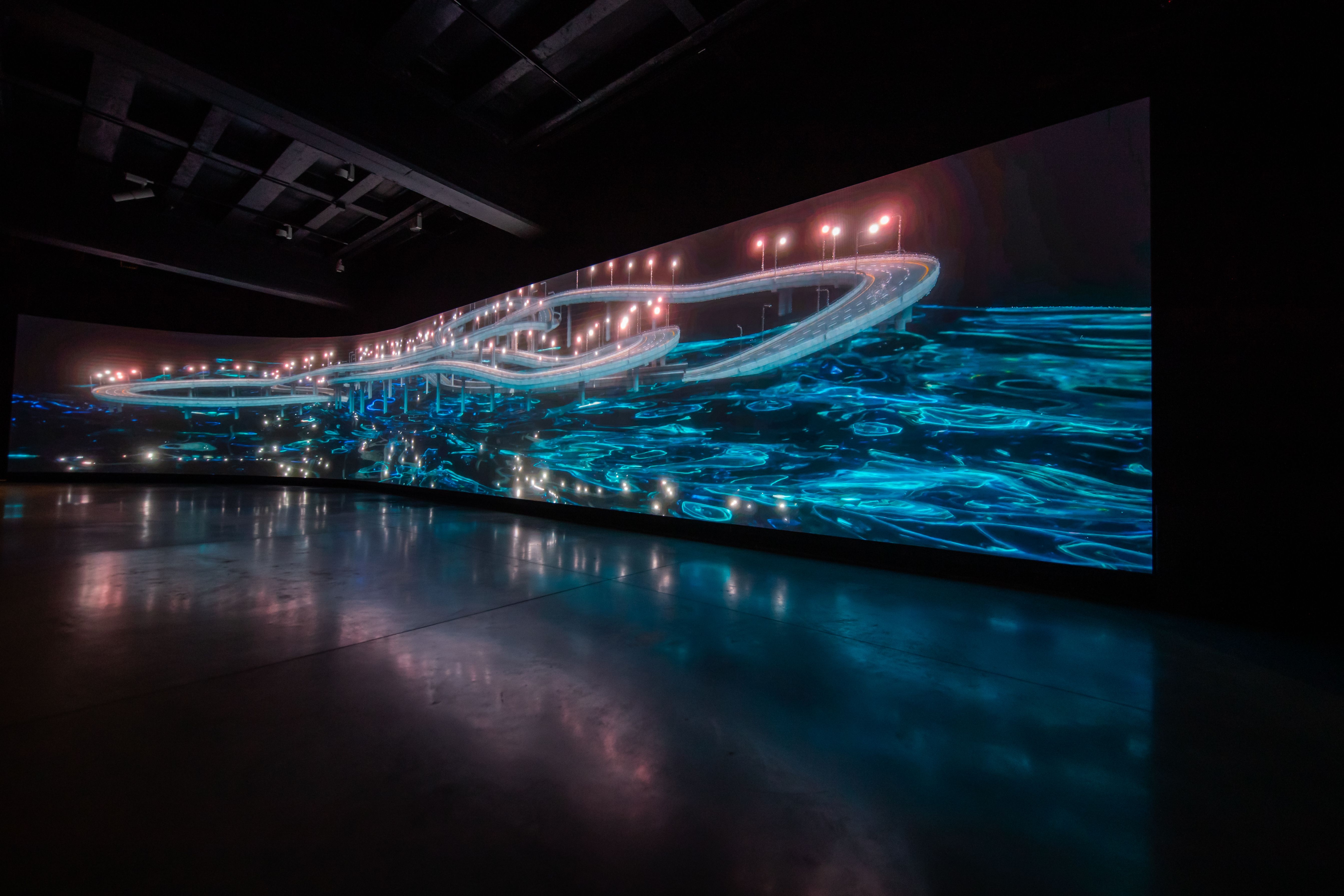 Dark room with large, glowing blue abstract highway projection.