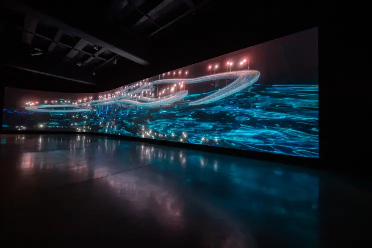 Dark room with large, glowing blue abstract highway projection.