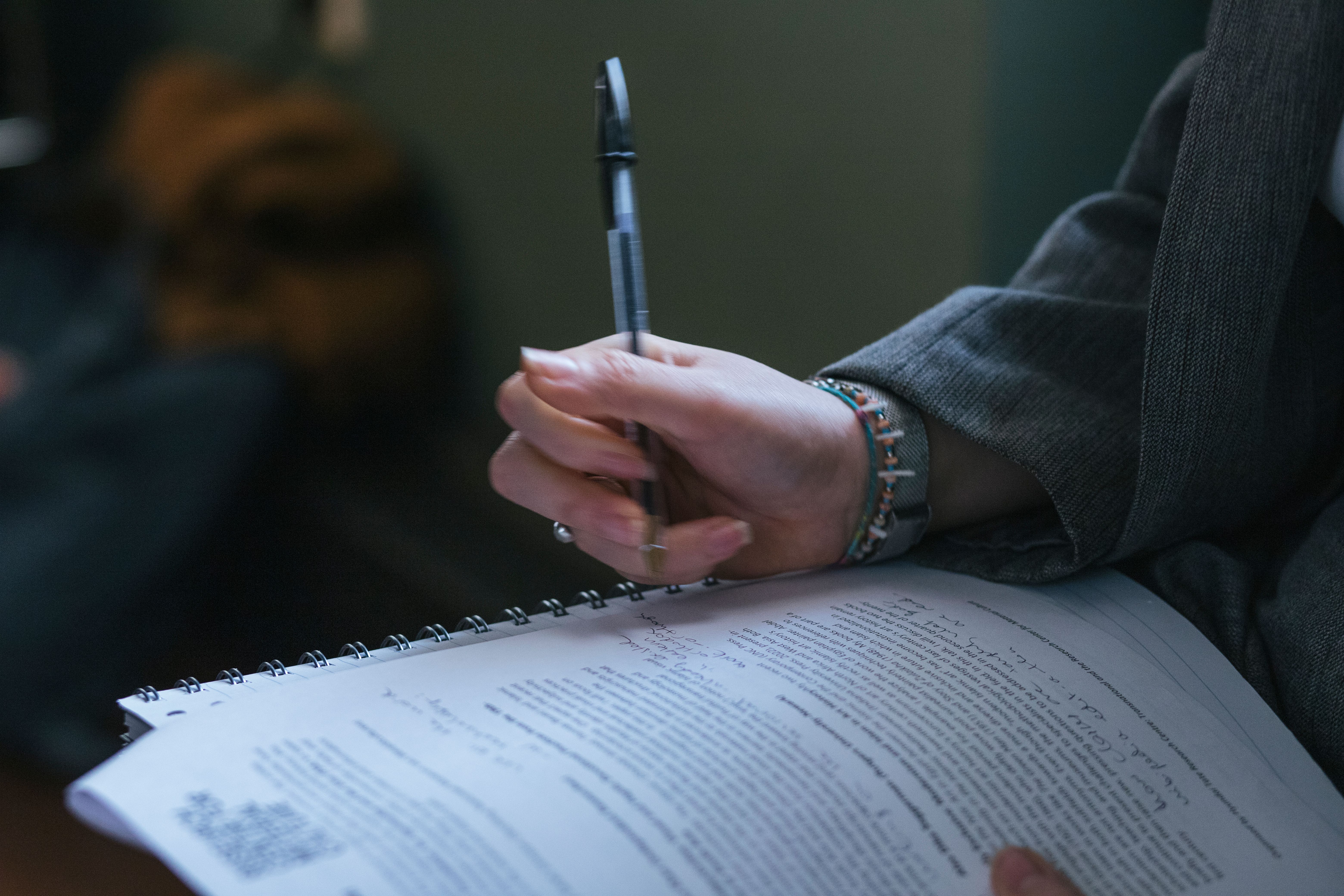 A hand adorned with a bracelet holding a pen, jotting down notes.