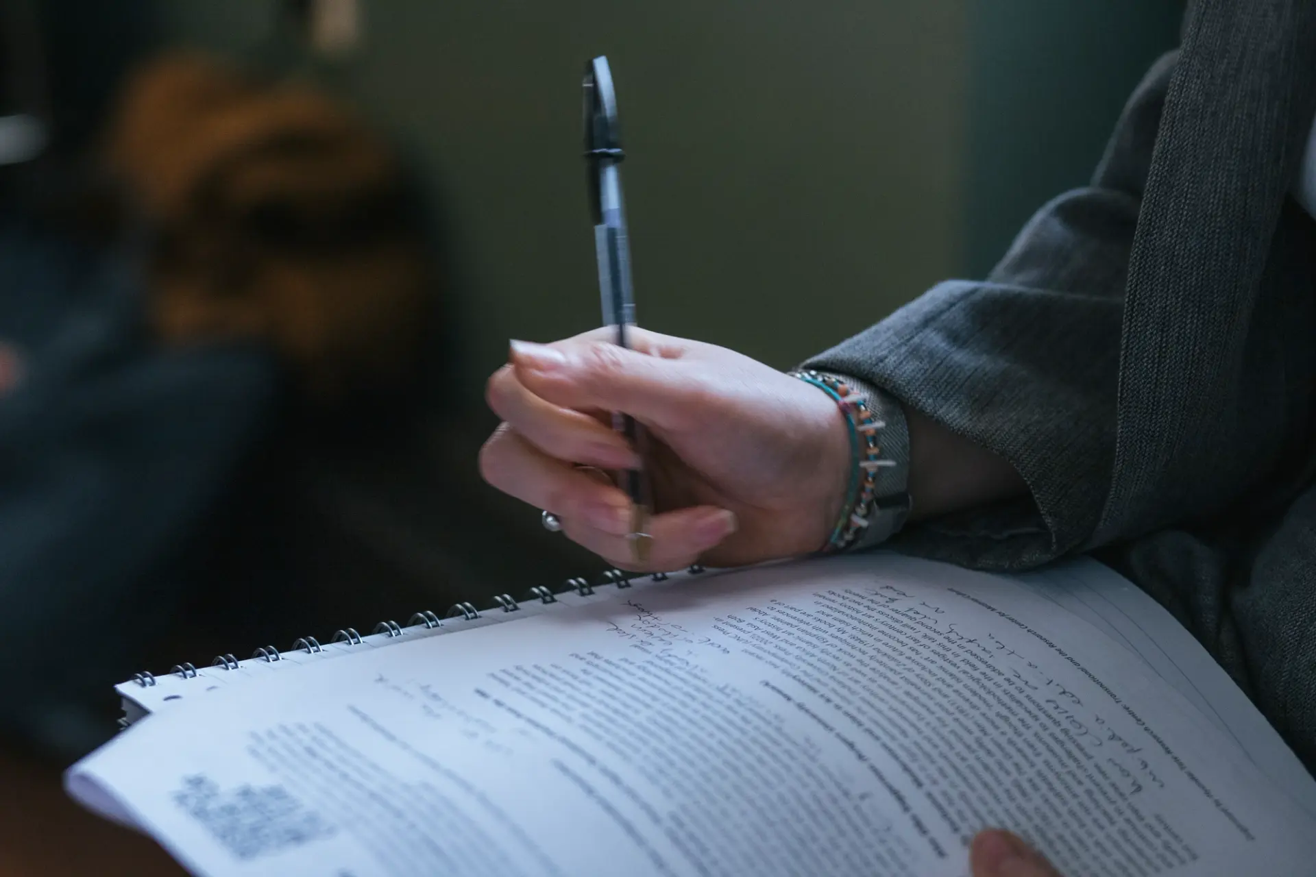 A hand adorned with a bracelet holding a pen, jotting down notes.