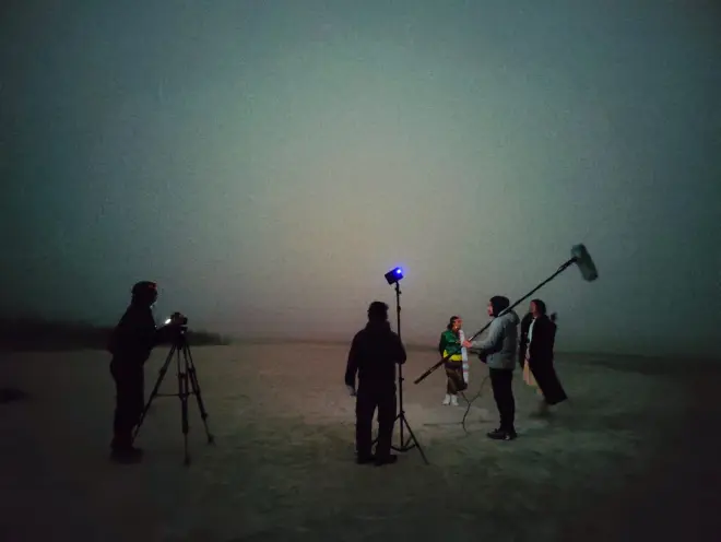 A filming team is at work in a field. The crew, equipped with professional video equipment, is focused on capturing a scen...